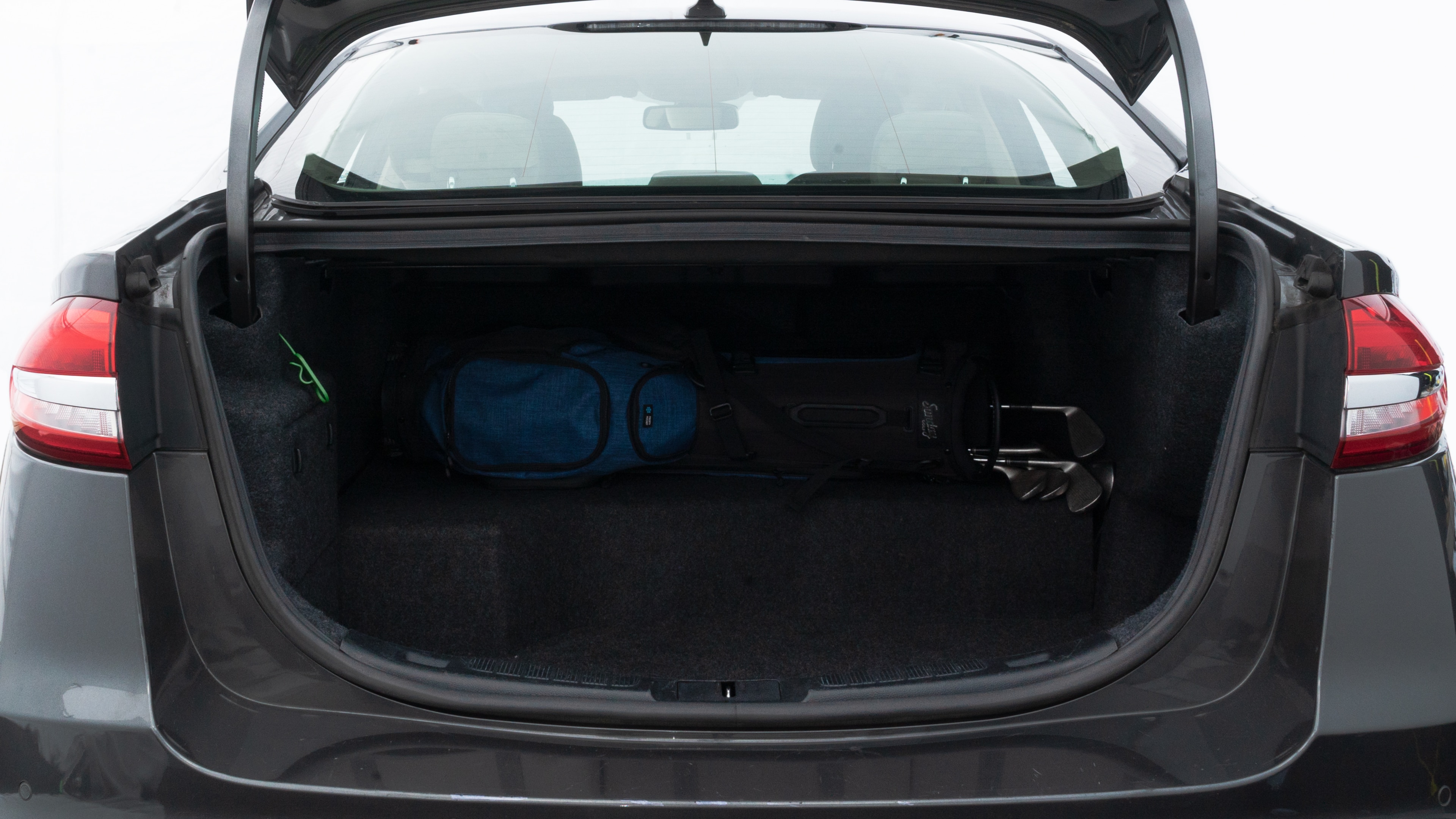 The trunk lid is open showing full view of the trunk. A baby stroller, three grocery carriers, two camping chairs in the carrying bag, and a set of golf clubs are placed inside.