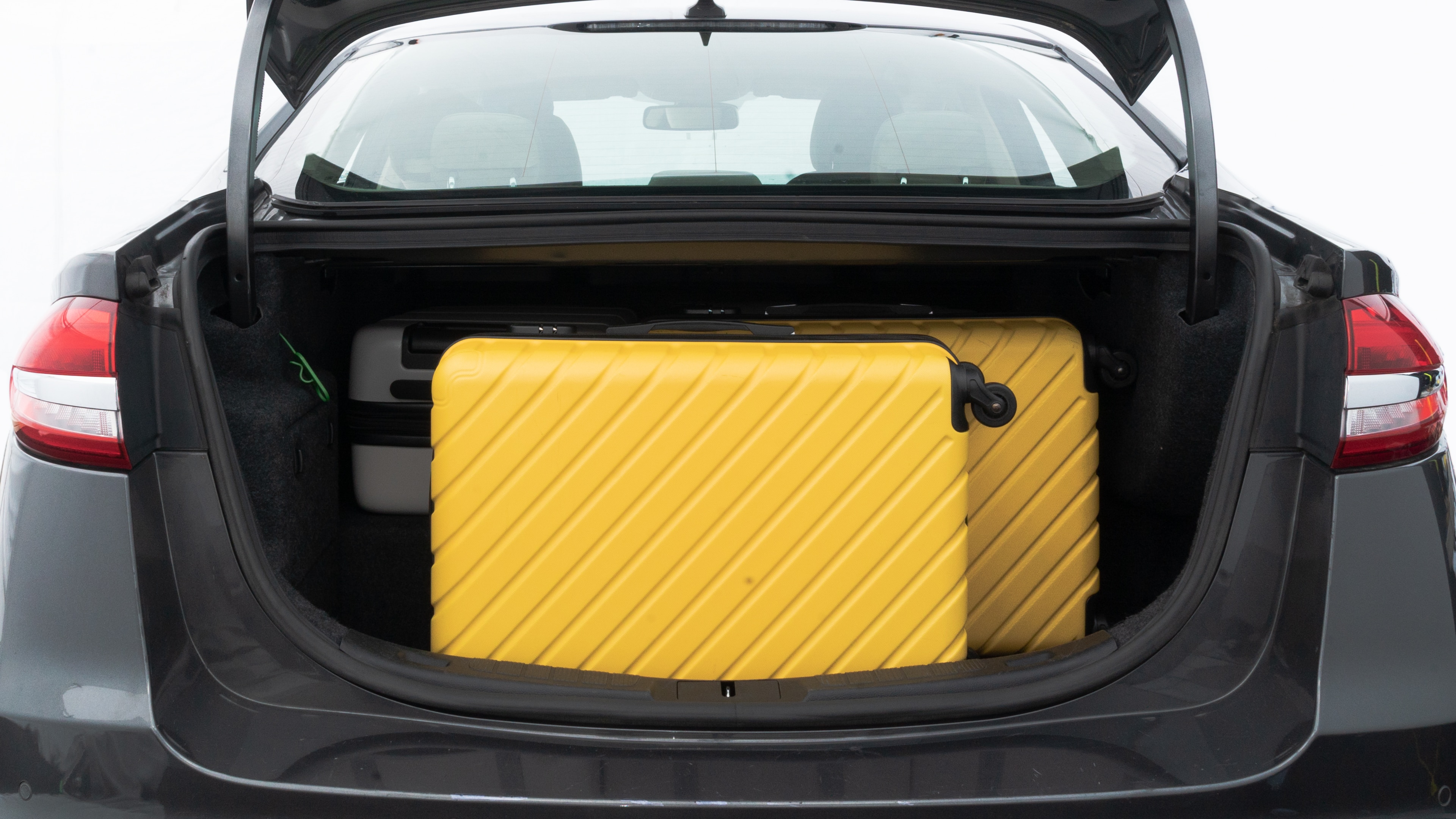 The trunk lid is open, showing full view of the trunk space. Two medium and two small suitcases are placed inside.