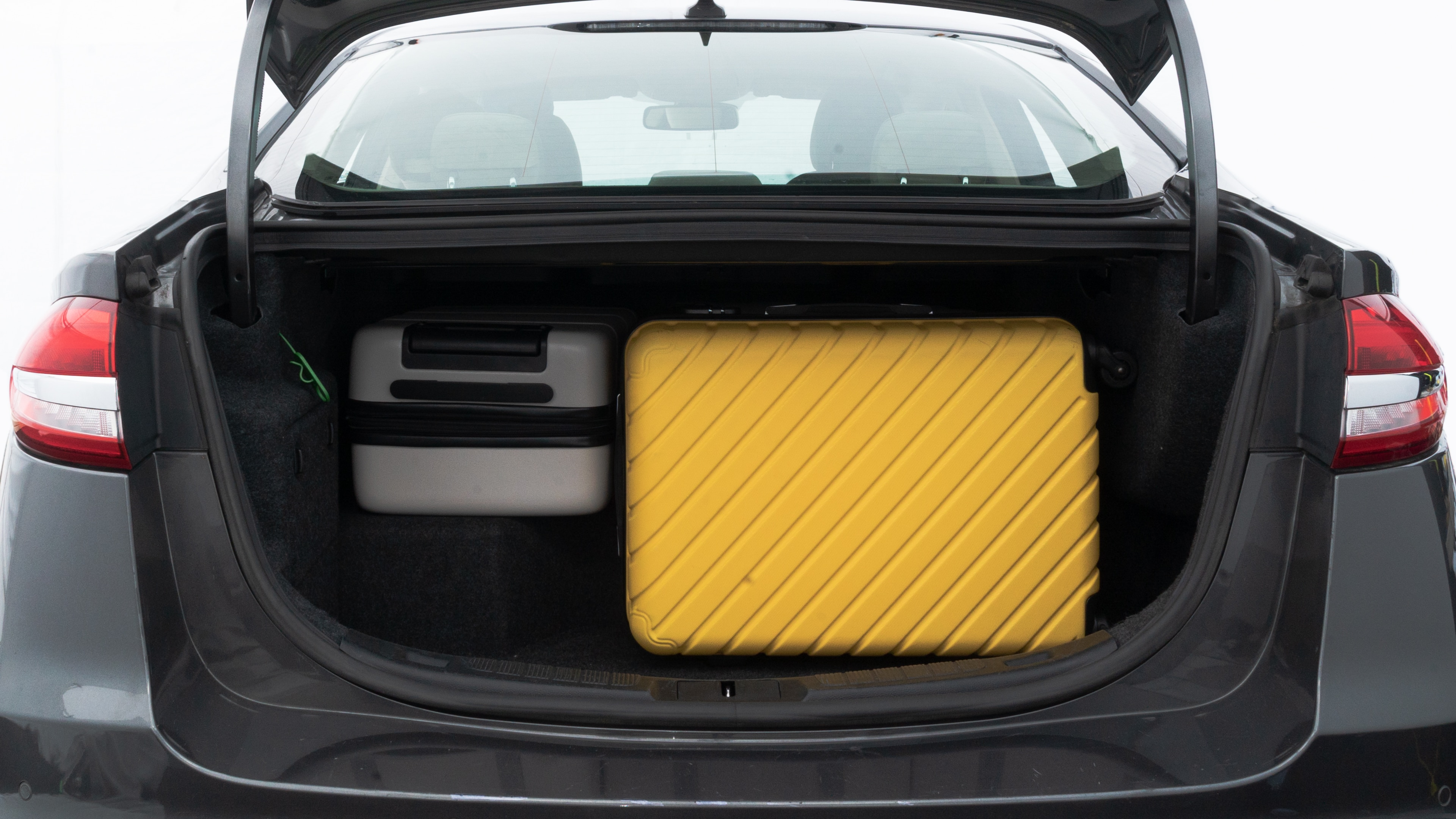 The trunk lid is open, showing full view of the trunk space. Two medium and two small suitcases are placed inside.