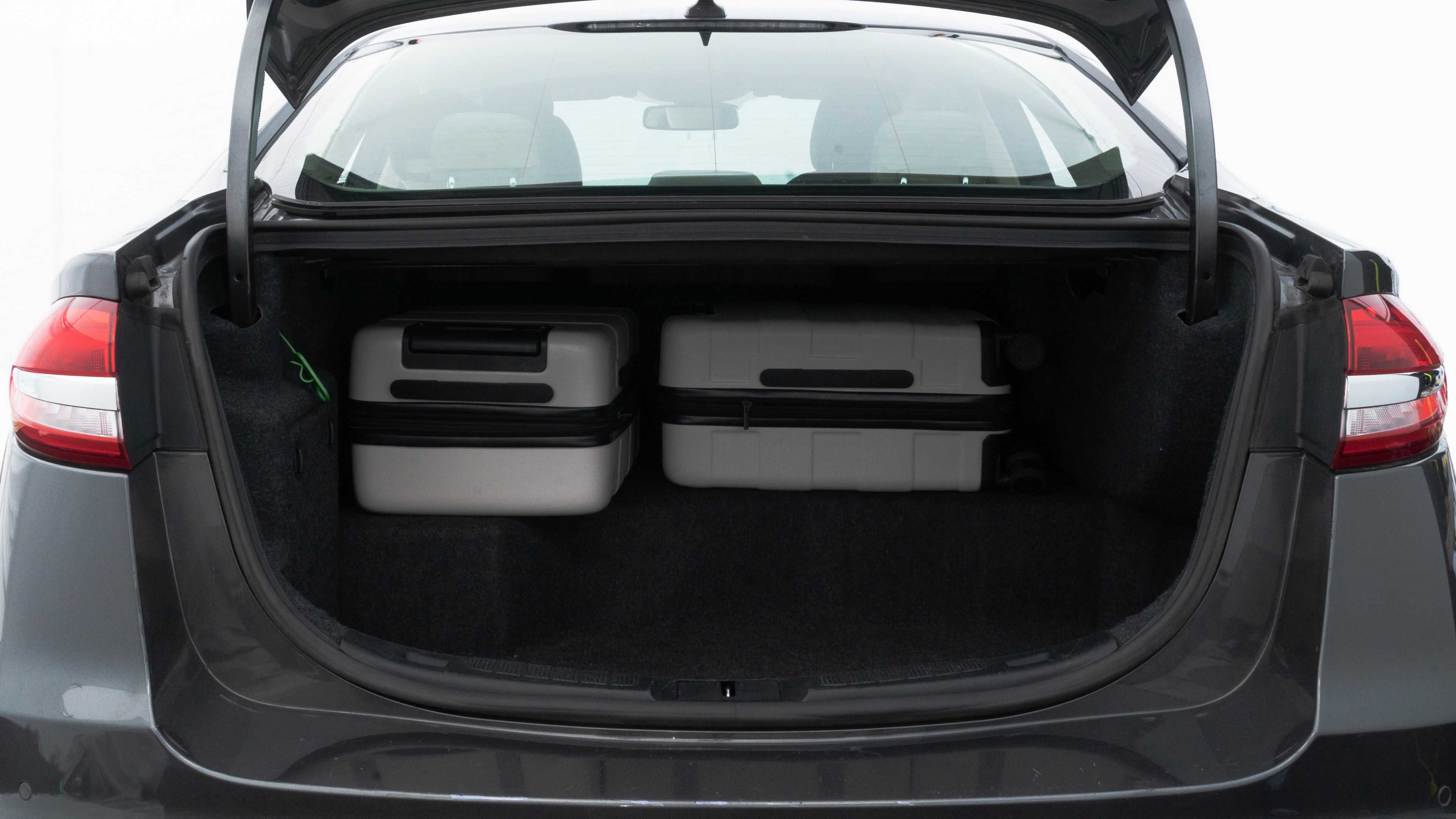 The trunk lid is open, showing full view of the trunk space. Two medium and two small suitcases are placed inside.