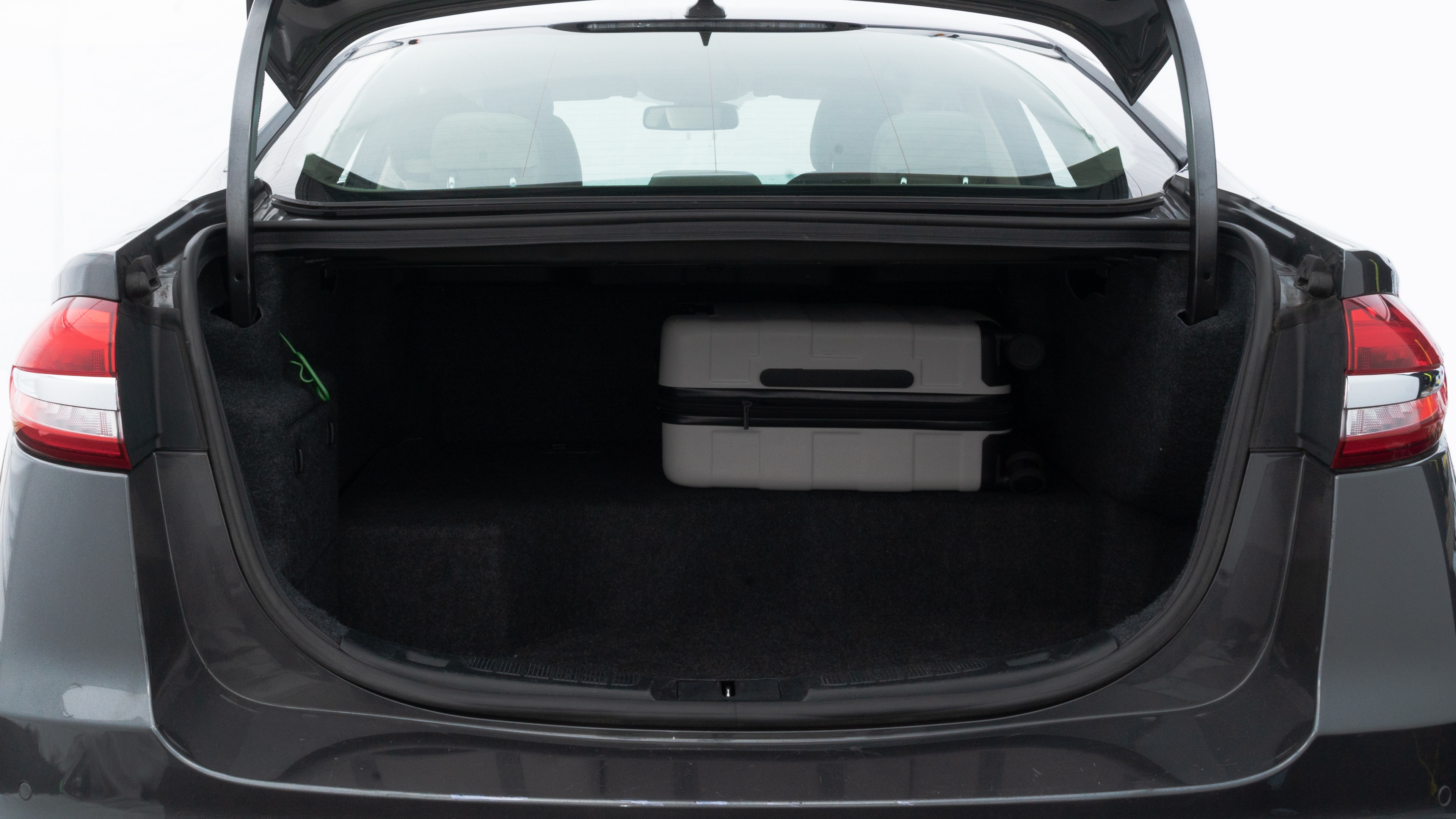 The trunk lid is open, showing full view of the trunk space. Two medium and two small suitcases are placed inside.