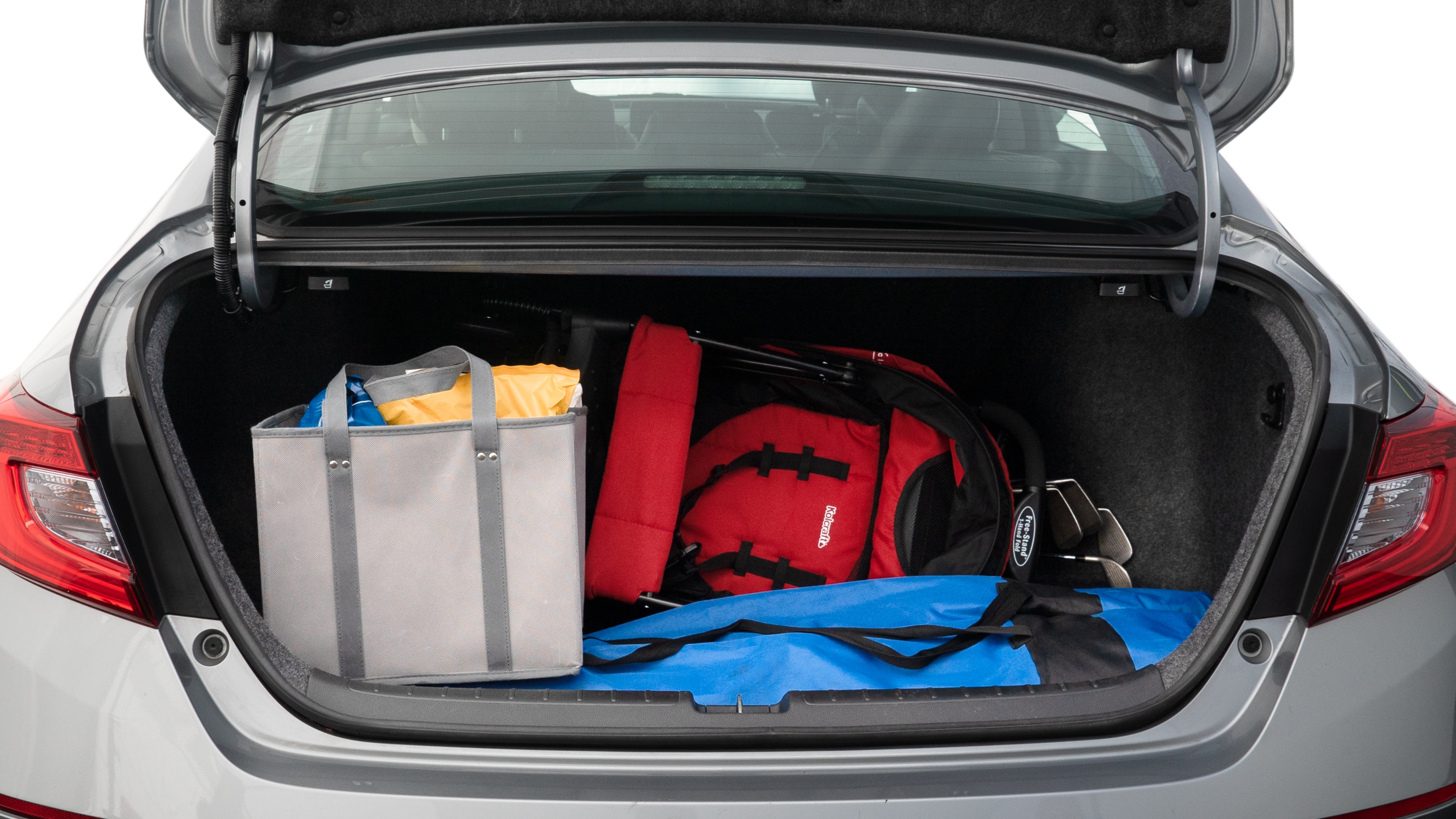 The trunk lid is open showing full view of the trunk. A baby stroller, three grocery carriers, two camping chairs in the carrying bag, and a set of golf clubs are placed inside.