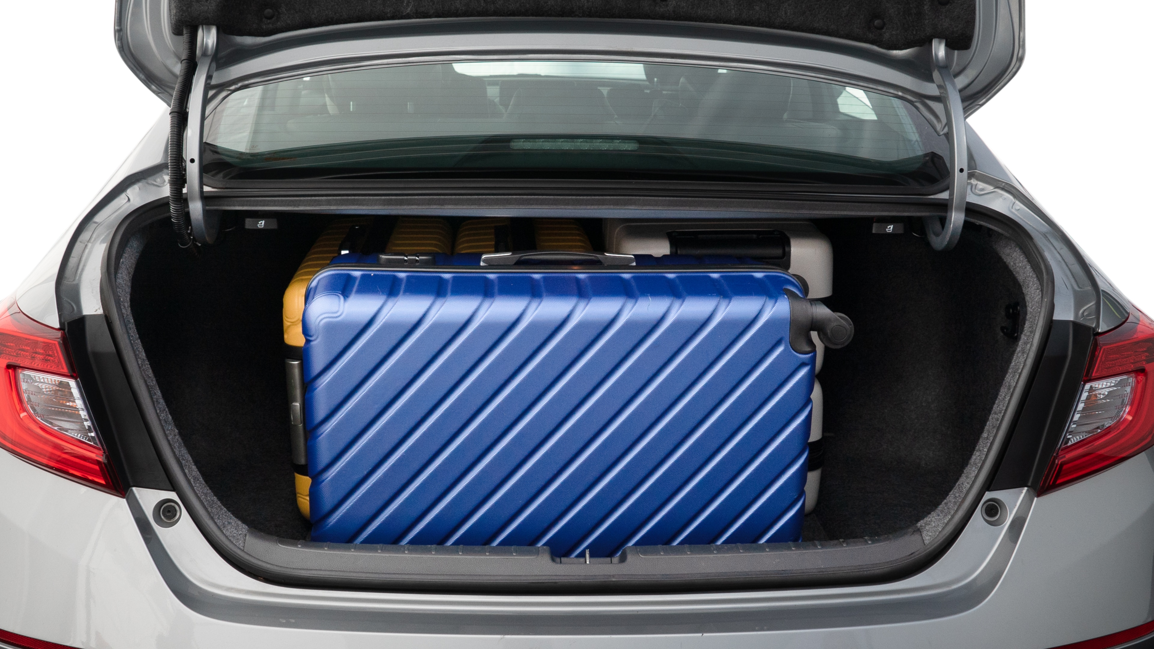 The trunk lid is open, showing full view of the trunk space. One large, two medium, and two small suitcases are placed inside.