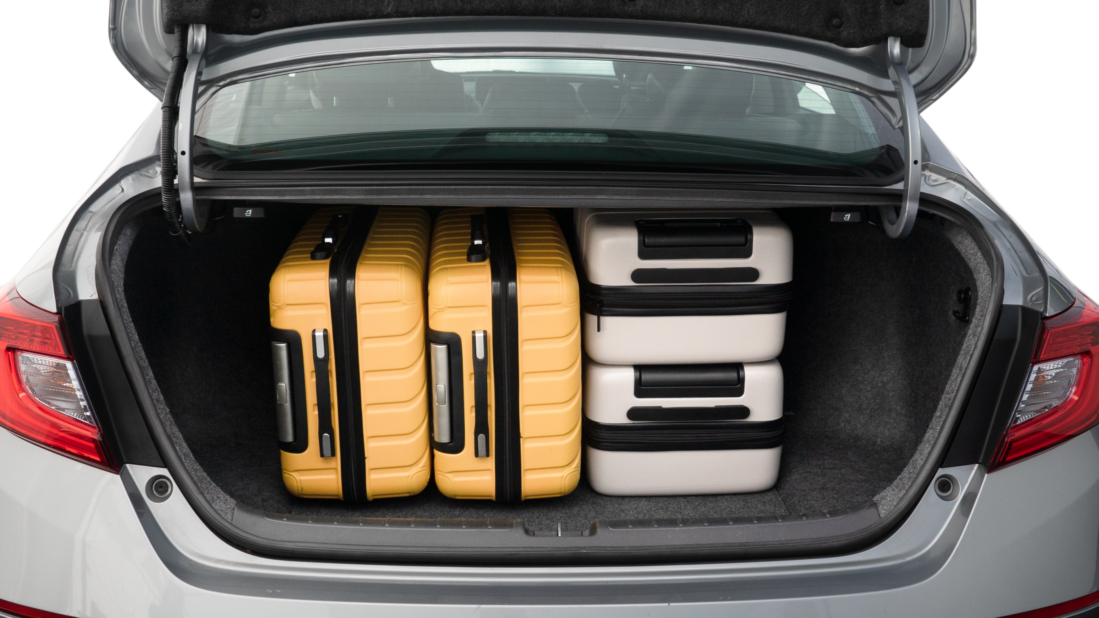 The trunk lid is open, showing full view of the trunk space. One large, two medium, and two small suitcases are placed inside.