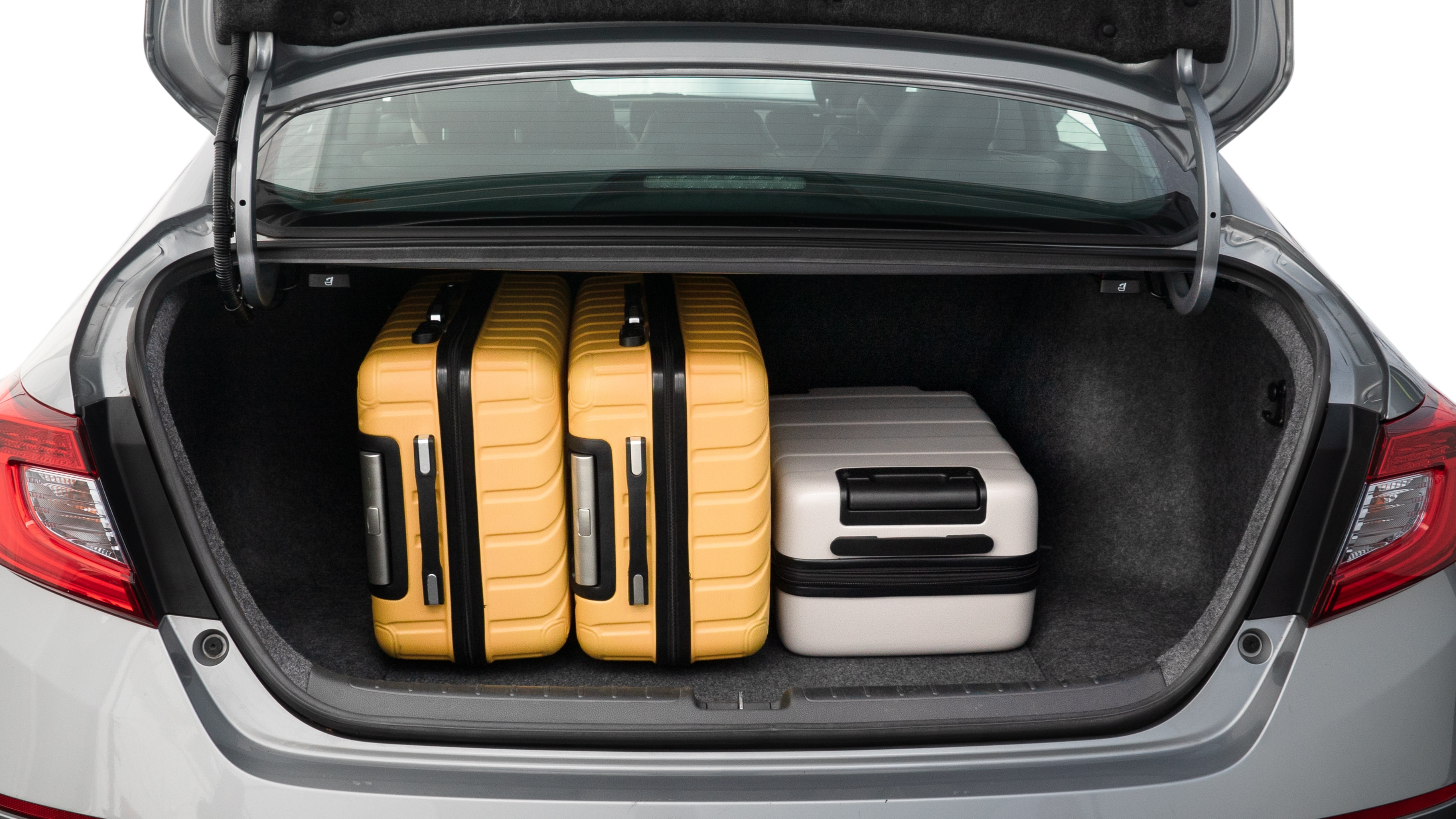 The trunk lid is open, showing full view of the trunk space. One large, two medium, and two small suitcases are placed inside.