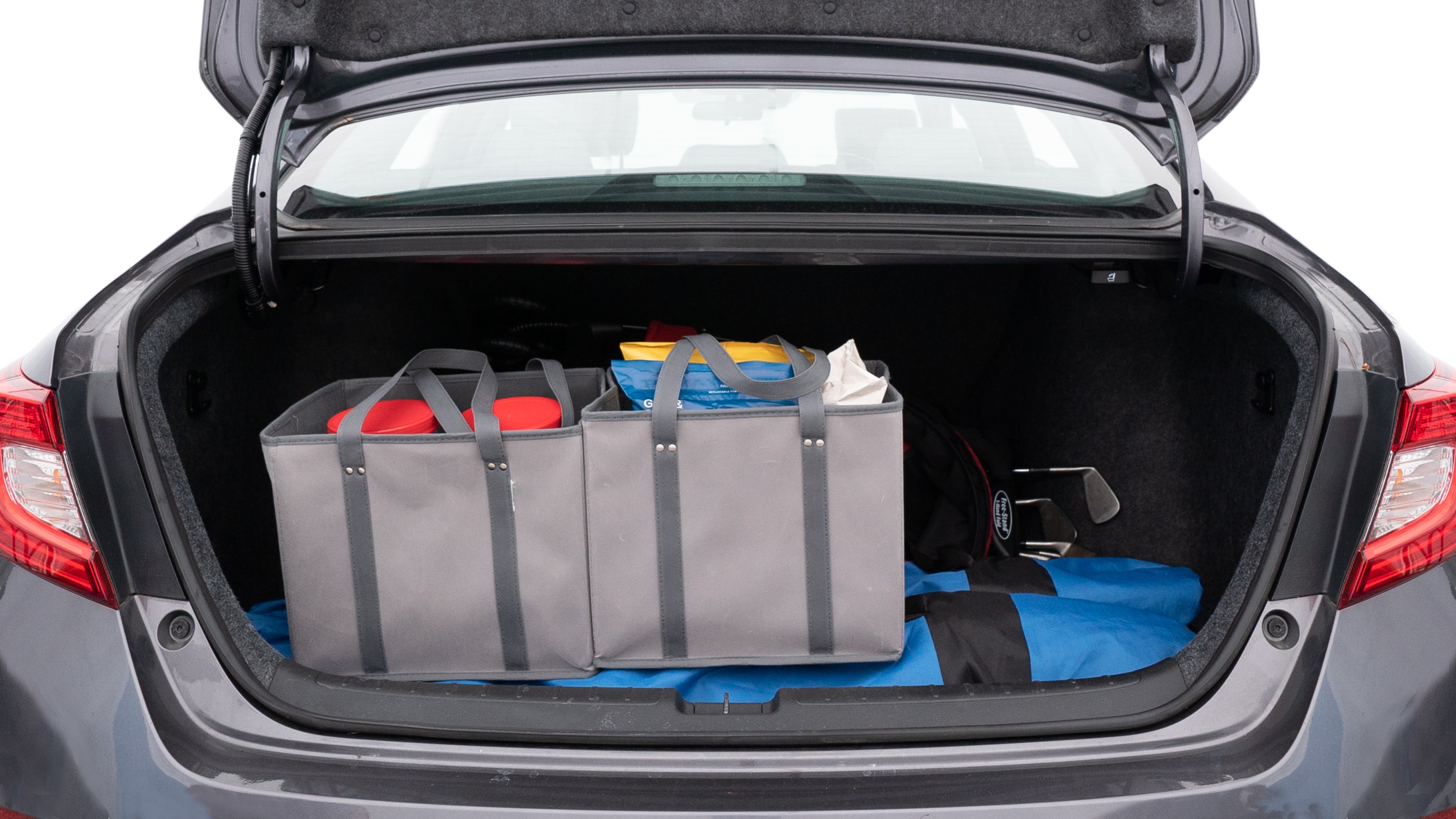 The trunk lid is open showing full view of the trunk. A baby stroller, three grocery carriers, two camping chairs in the carrying bag, and a set of golf clubs are placed inside.