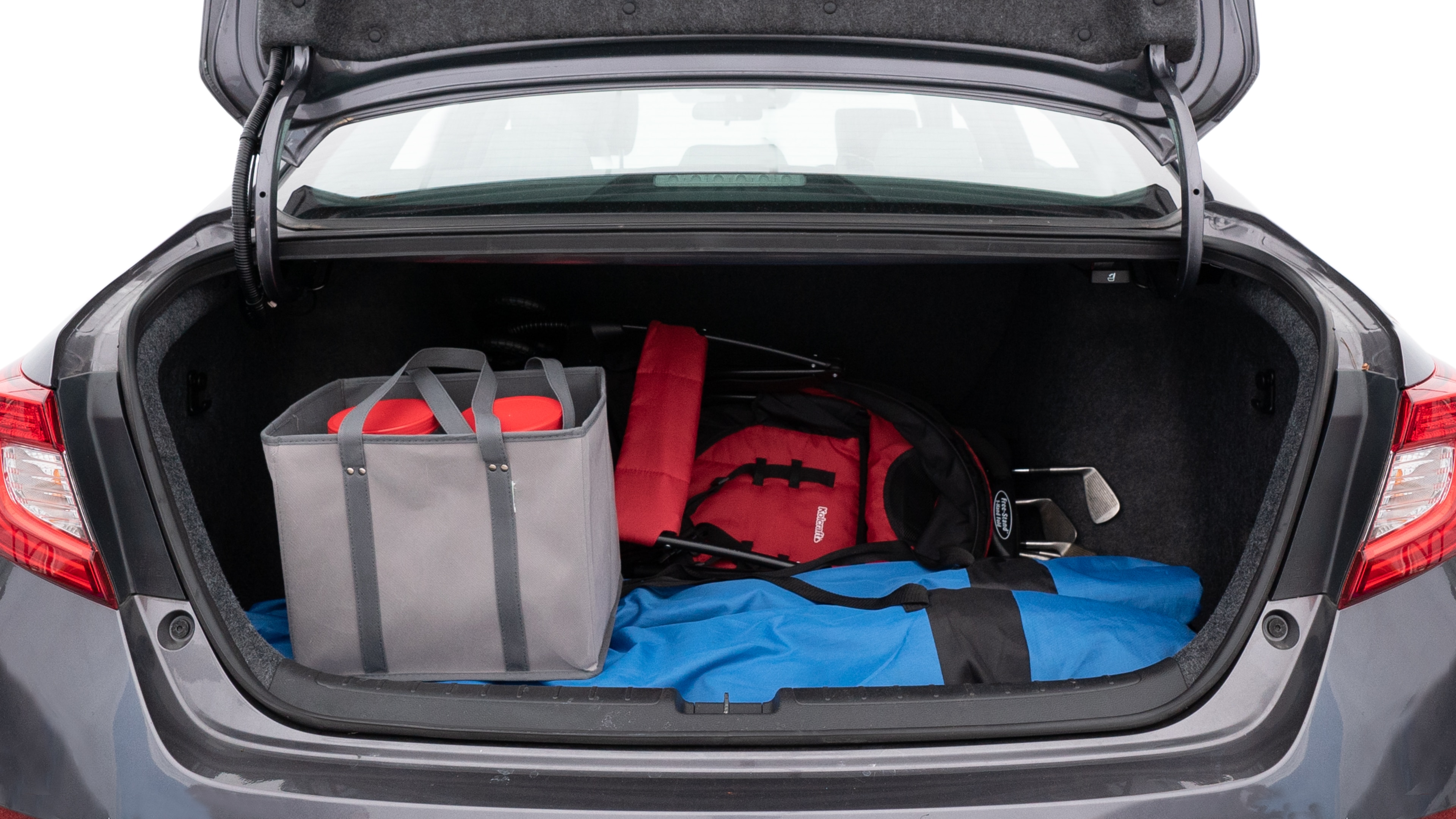 The trunk lid is open showing full view of the trunk. A baby stroller, three grocery carriers, two camping chairs in the carrying bag, and a set of golf clubs are placed inside.