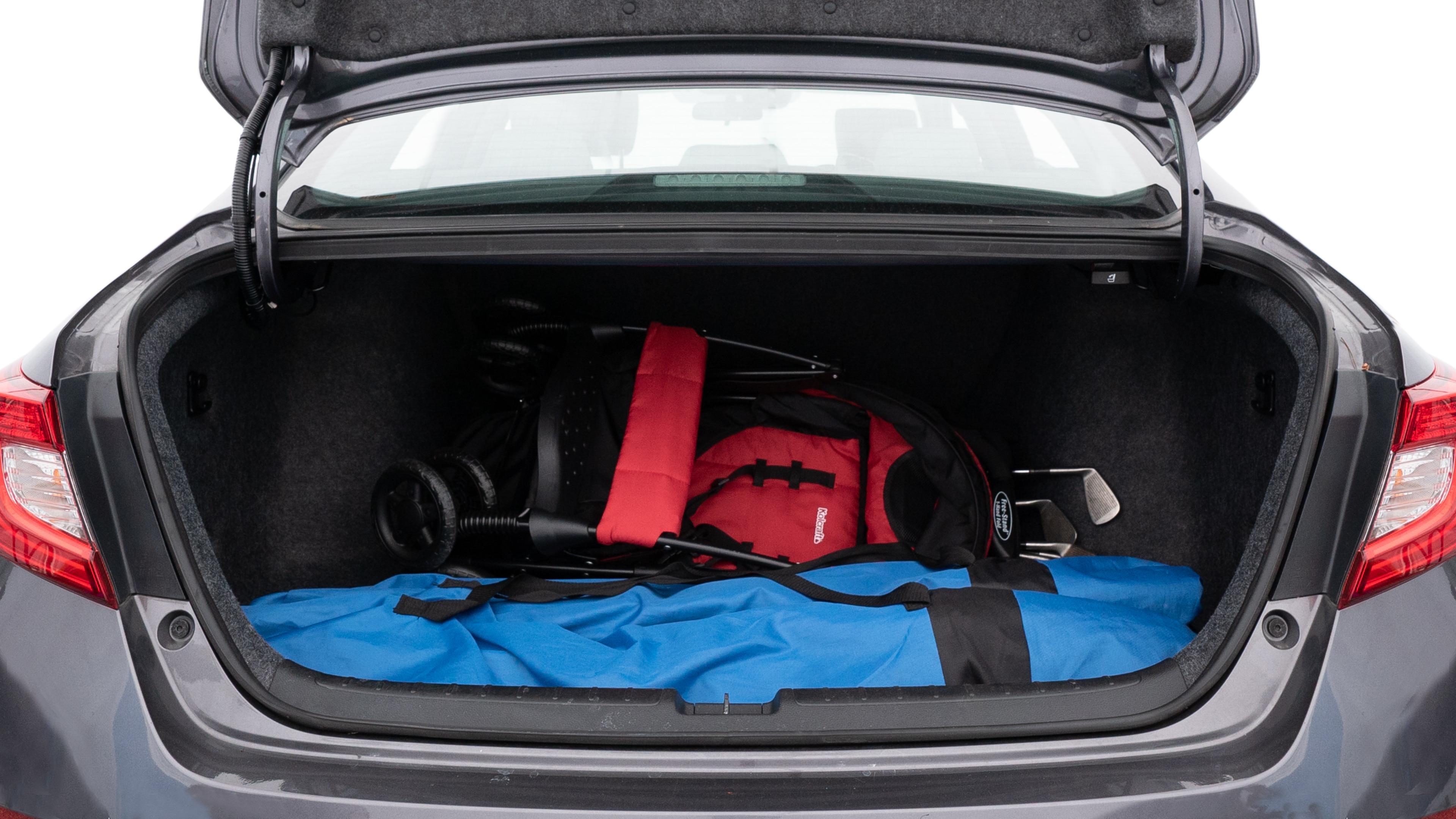 The trunk lid is open showing full view of the trunk. A baby stroller, three grocery carriers, two camping chairs in the carrying bag, and a set of golf clubs are placed inside.