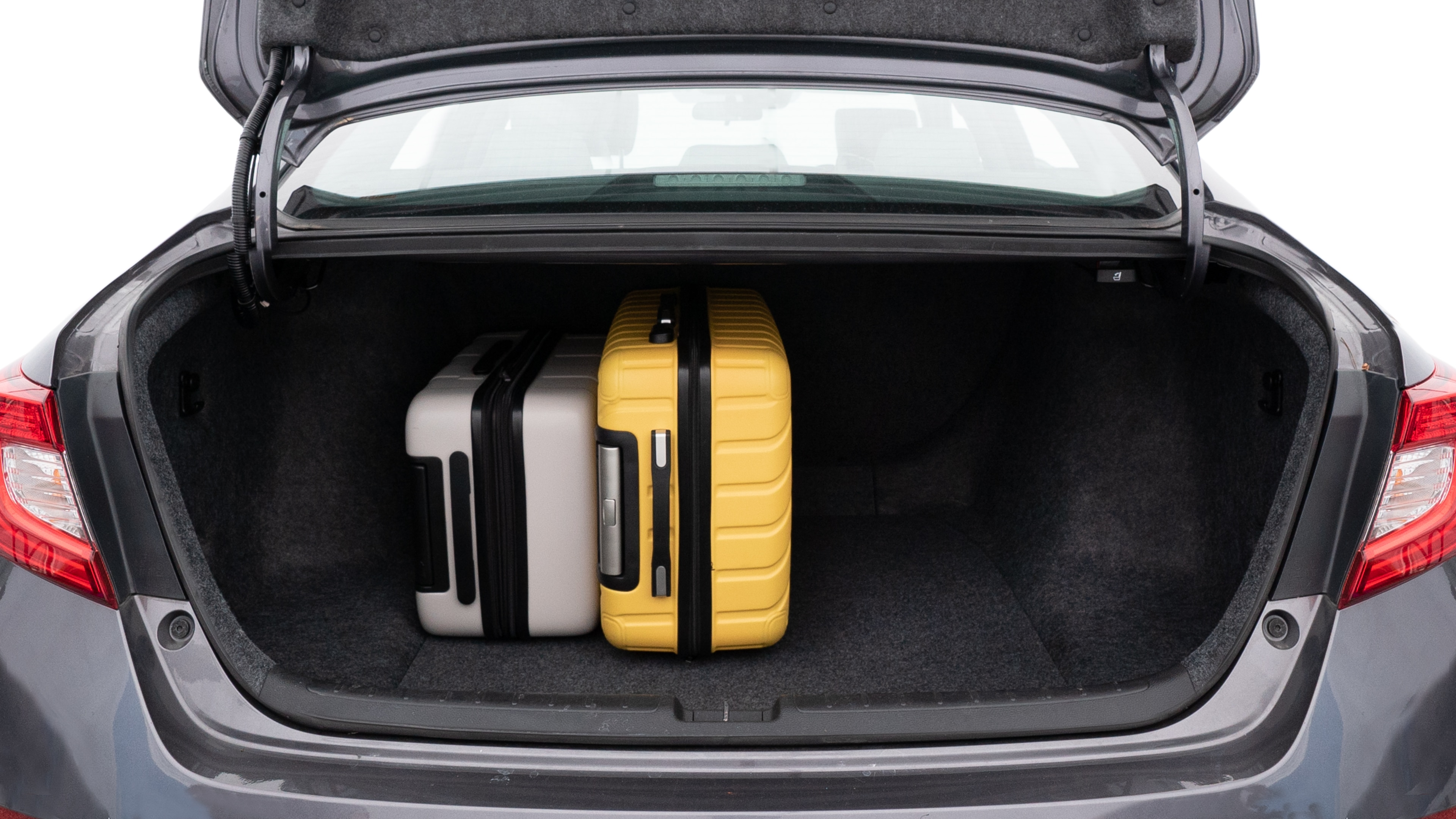 The trunk lid is open, showing full view of the trunk space. One large, two medium, and one small suitcases are placed inside.