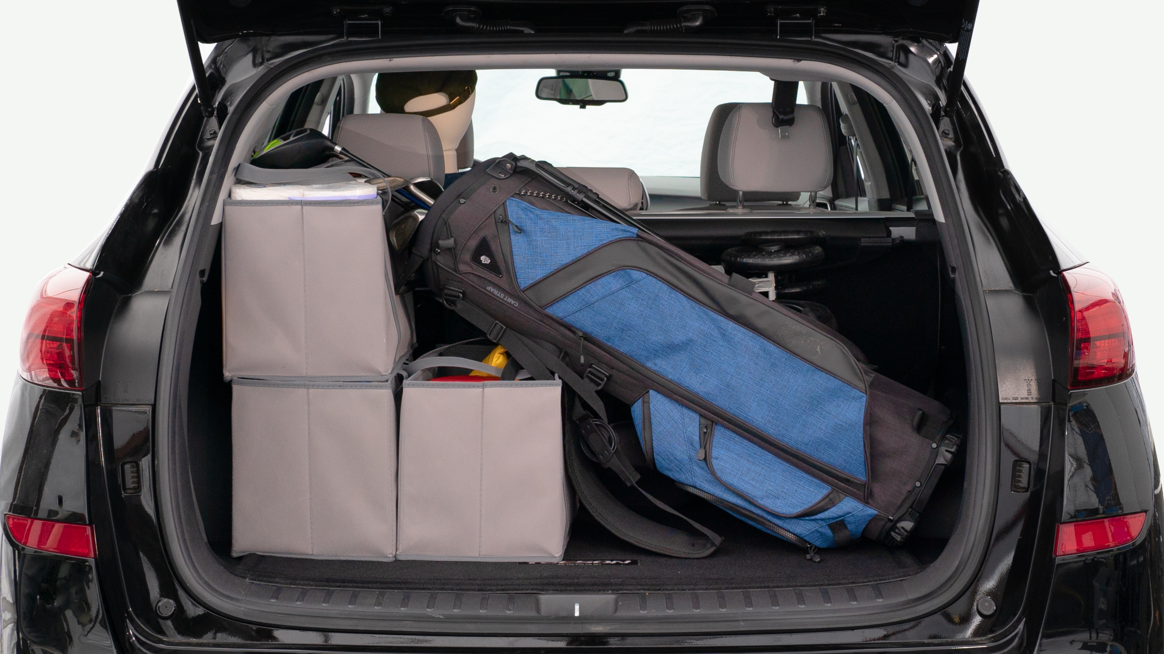 The trunk lid is open showing full view of the trunk. A baby stroller, three grocery carriers, and a set of golf clubs are placed inside.