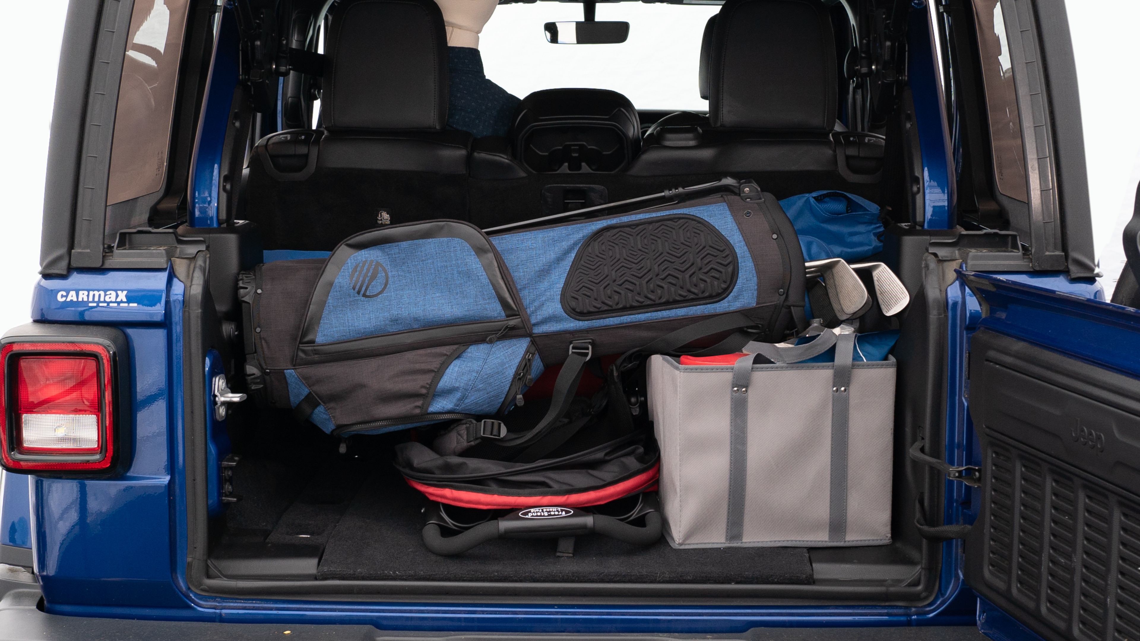 The trunk lid is open showing full view of the trunk. A baby stroller, three grocery carriers, two camping chairs in the carrying bag, and a set of golf clubs are placed inside.