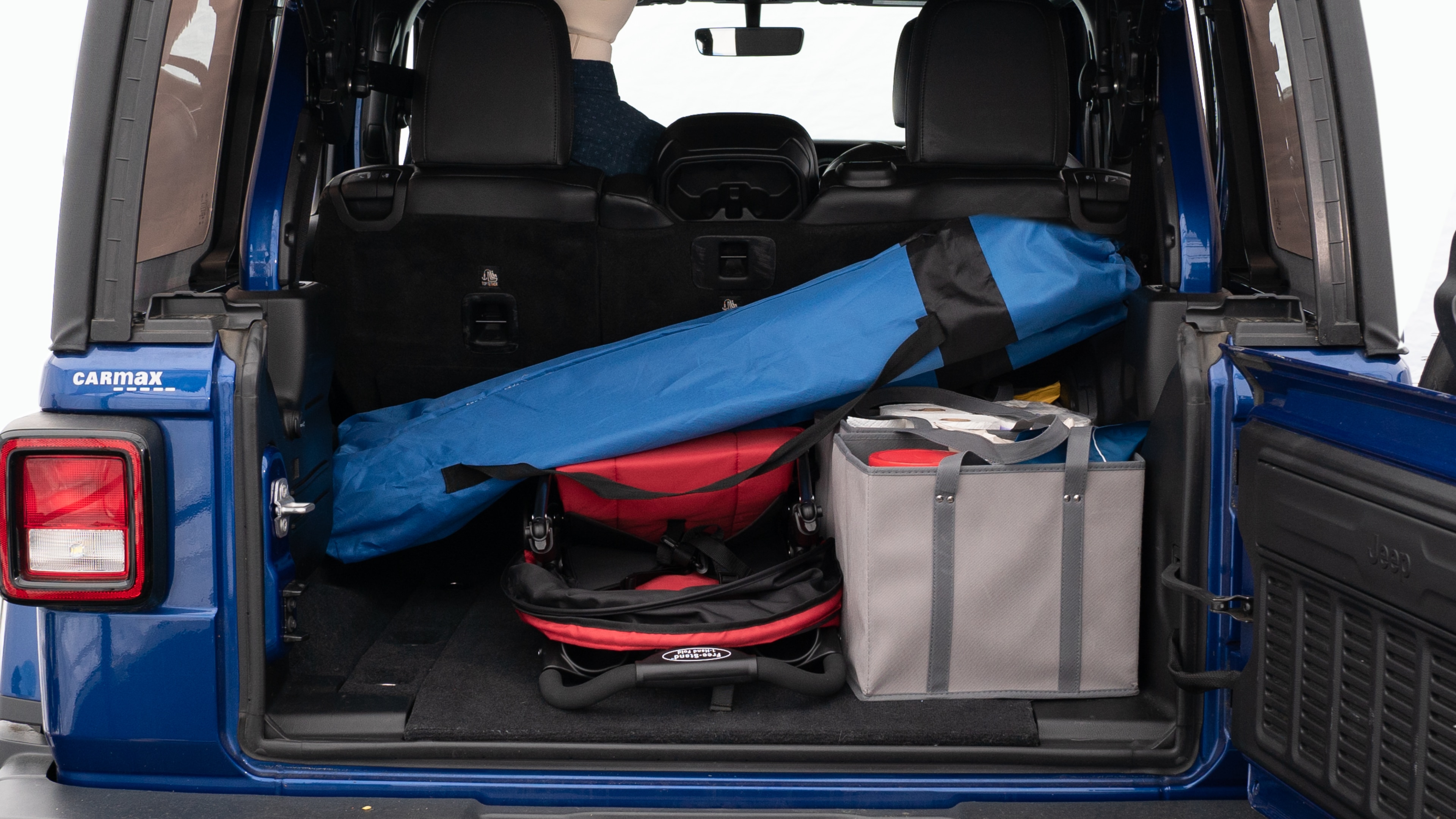 The trunk lid is open showing full view of the trunk. A baby stroller, three grocery carriers, two camping chairs in the carrying bag, and a set of golf clubs are placed inside.