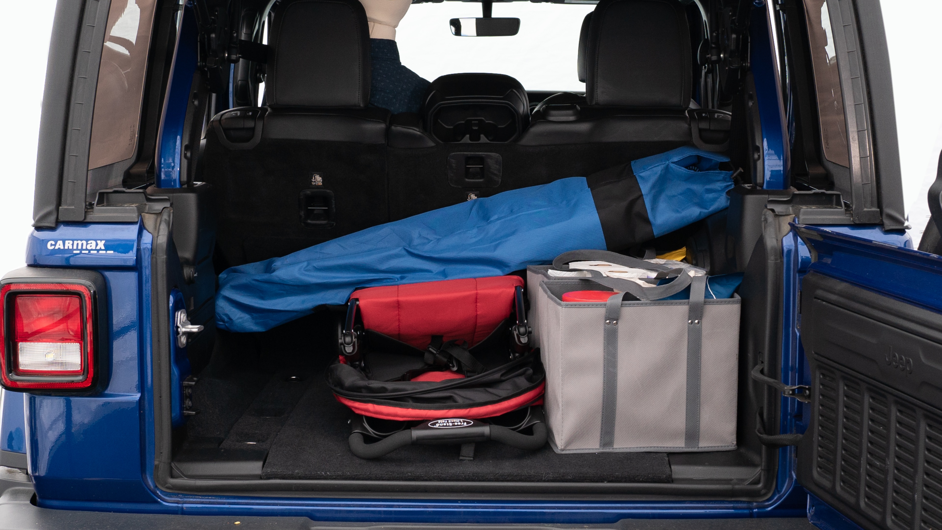The trunk lid is open showing full view of the trunk. A baby stroller, three grocery carriers, two camping chairs in the carrying bag, and a set of golf clubs are placed inside.