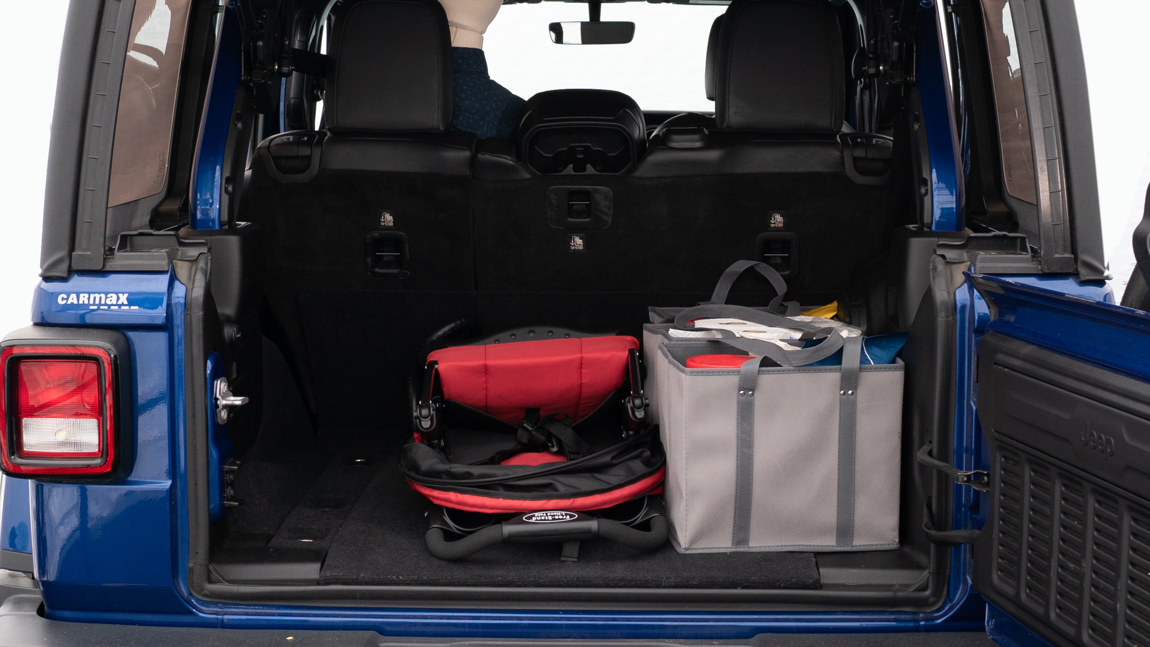 The trunk lid is open showing full view of the trunk. A baby stroller, three grocery carriers, two camping chairs in the carrying bag, and a set of golf clubs are placed inside.