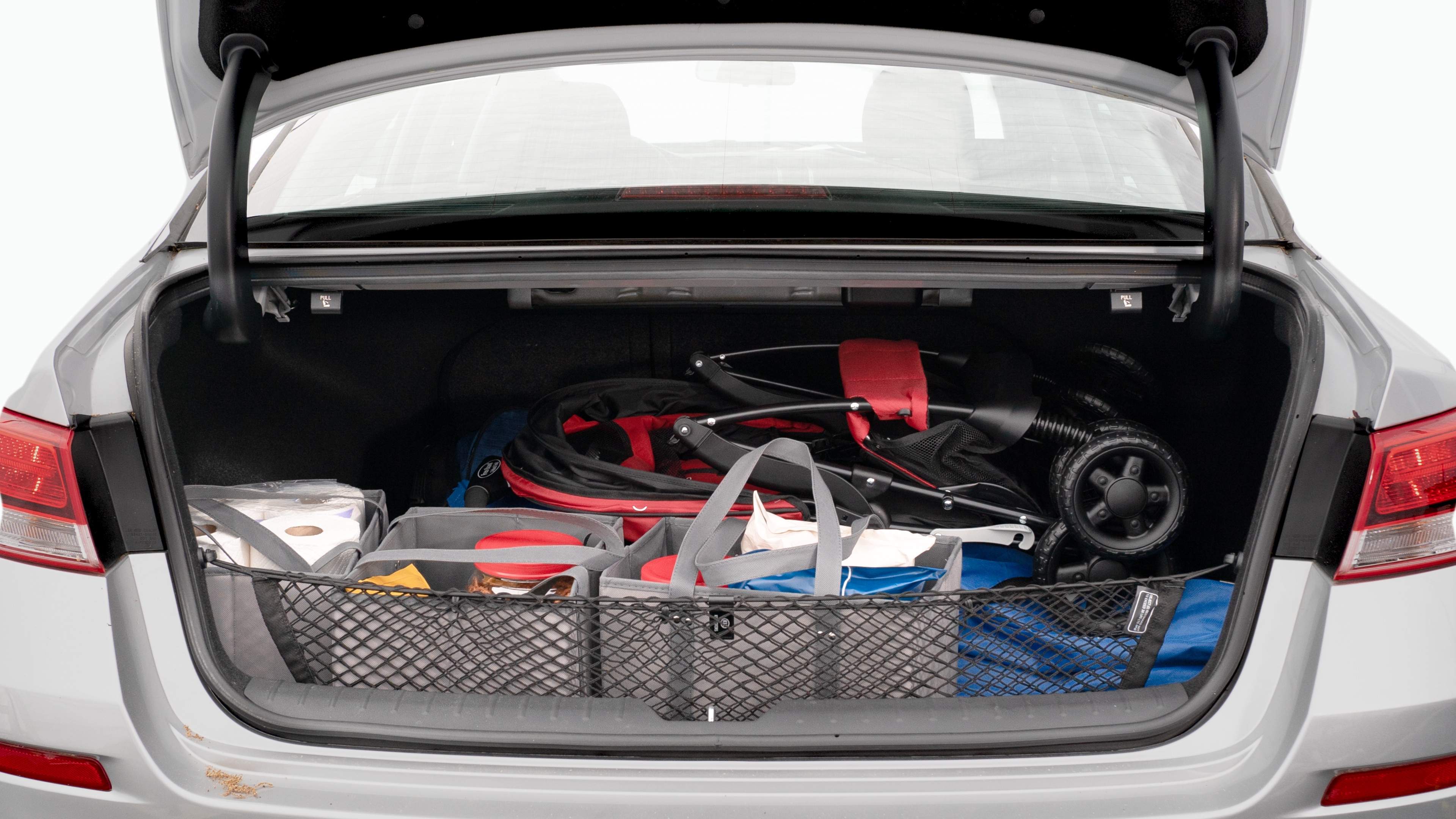 The trunk lid is open showing full view of the trunk. A baby stroller, three grocery carriers, two camping chairs in the carrying bag, and a set of golf clubs are placed inside.