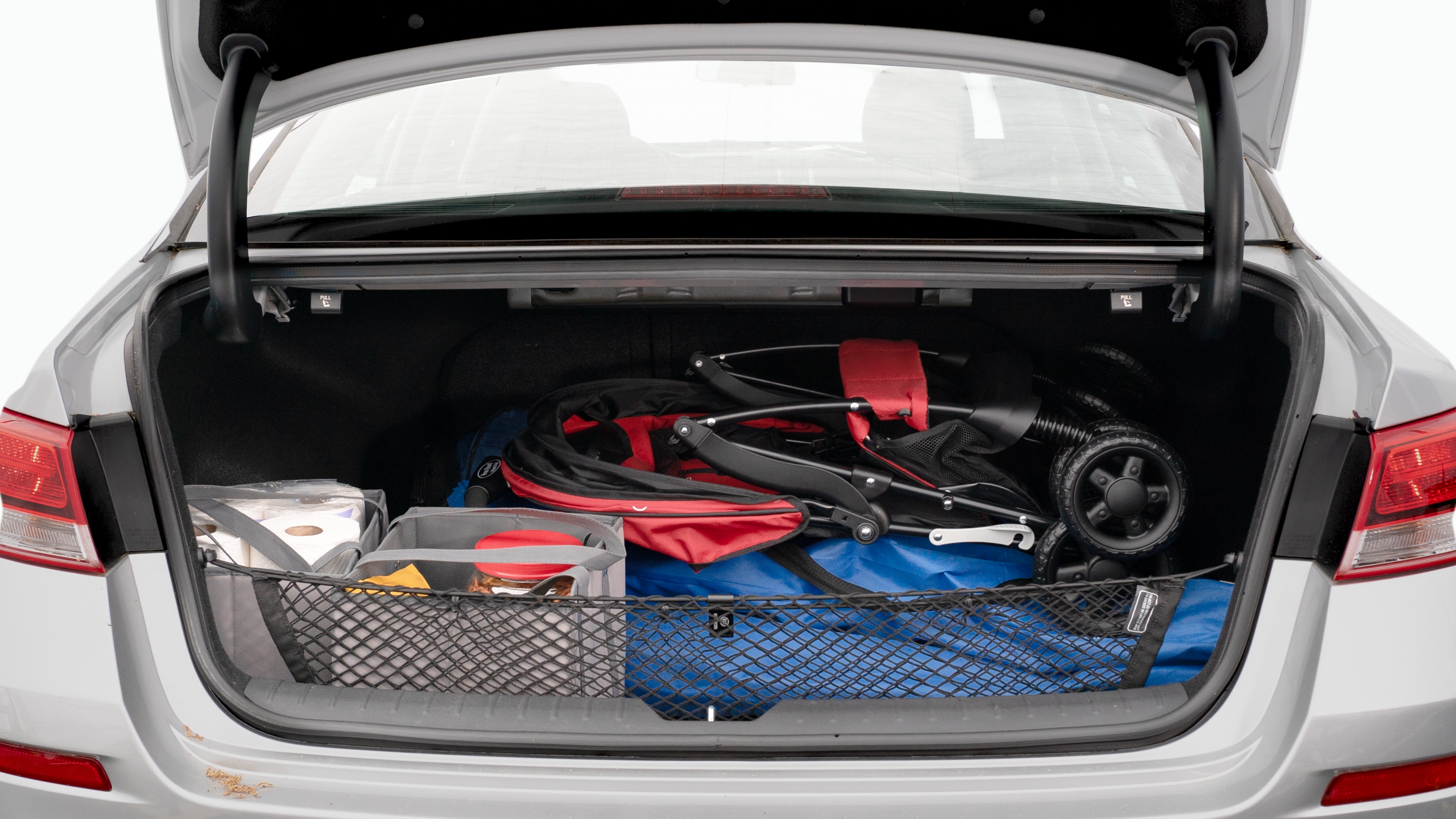 The trunk lid is open showing full view of the trunk. A baby stroller, three grocery carriers, two camping chairs in the carrying bag, and a set of golf clubs are placed inside.