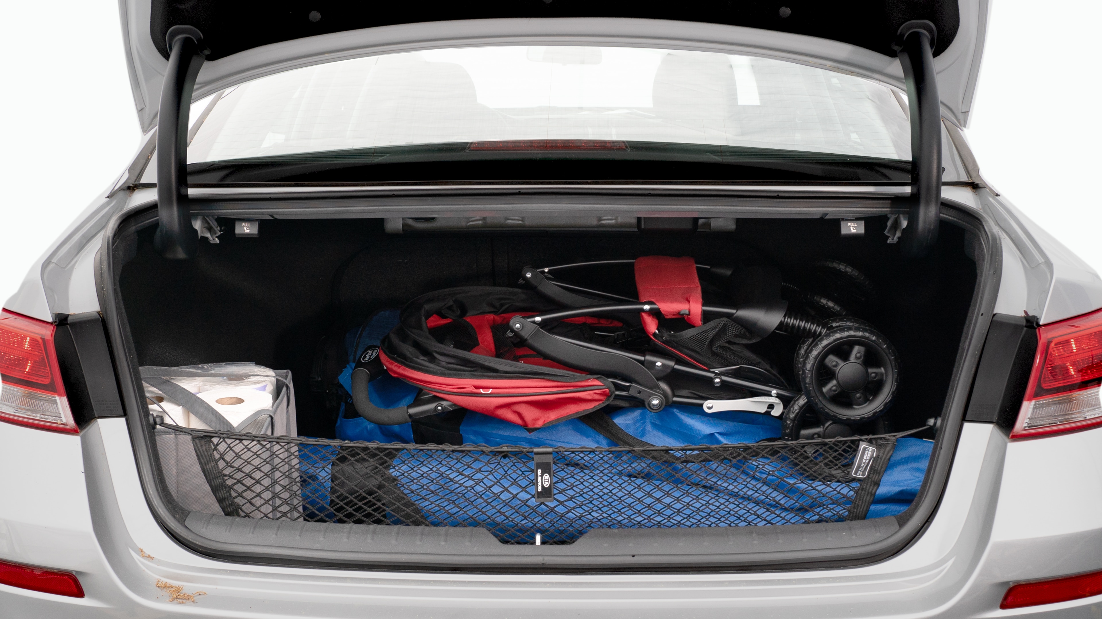 The trunk lid is open showing full view of the trunk. A baby stroller, three grocery carriers, two camping chairs in the carrying bag, and a set of golf clubs are placed inside.