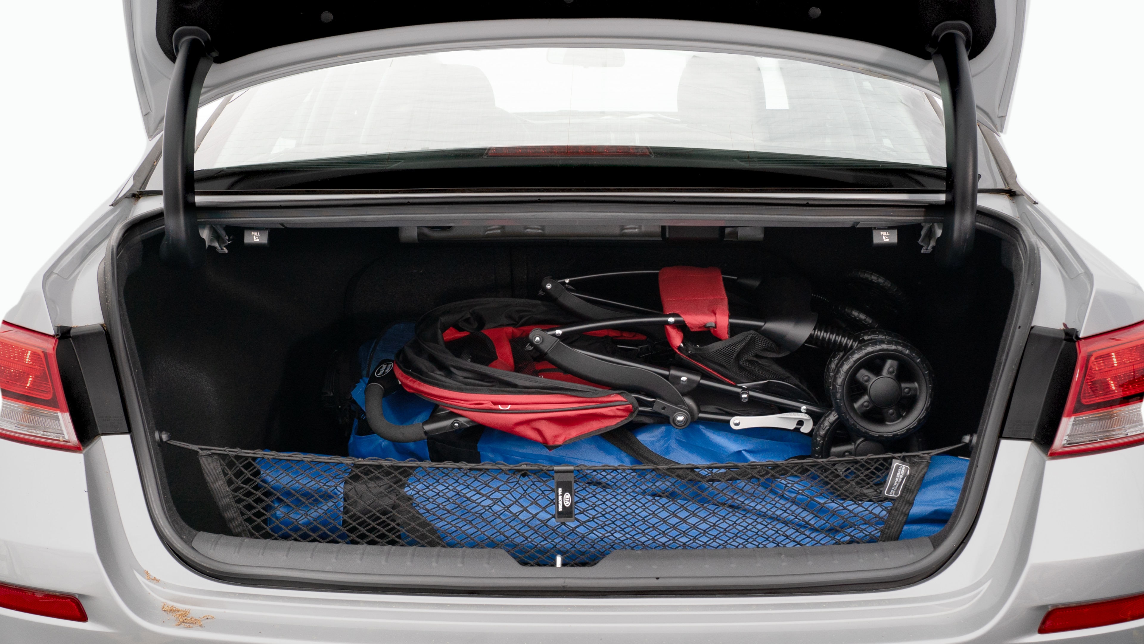 The trunk lid is open showing full view of the trunk. A baby stroller, three grocery carriers, two camping chairs in the carrying bag, and a set of golf clubs are placed inside.