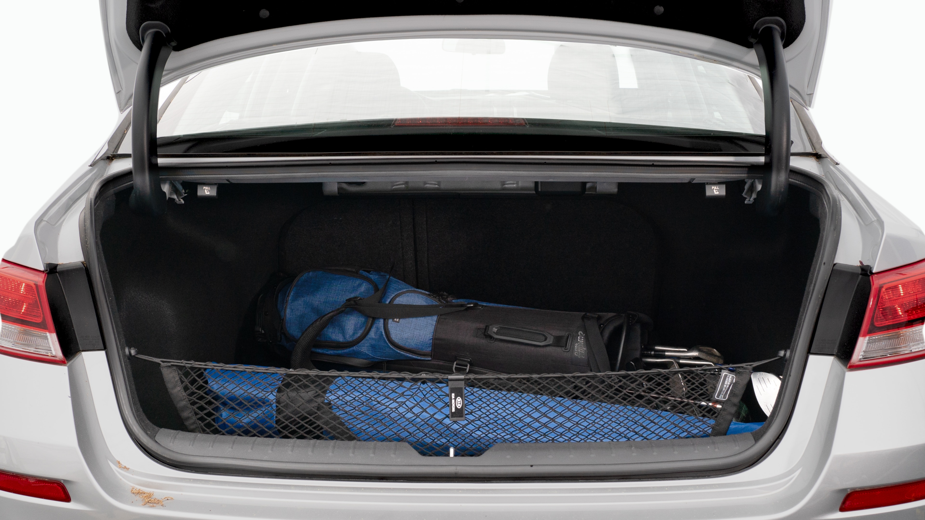 The trunk lid is open showing full view of the trunk. A baby stroller, three grocery carriers, two camping chairs in the carrying bag, and a set of golf clubs are placed inside.
