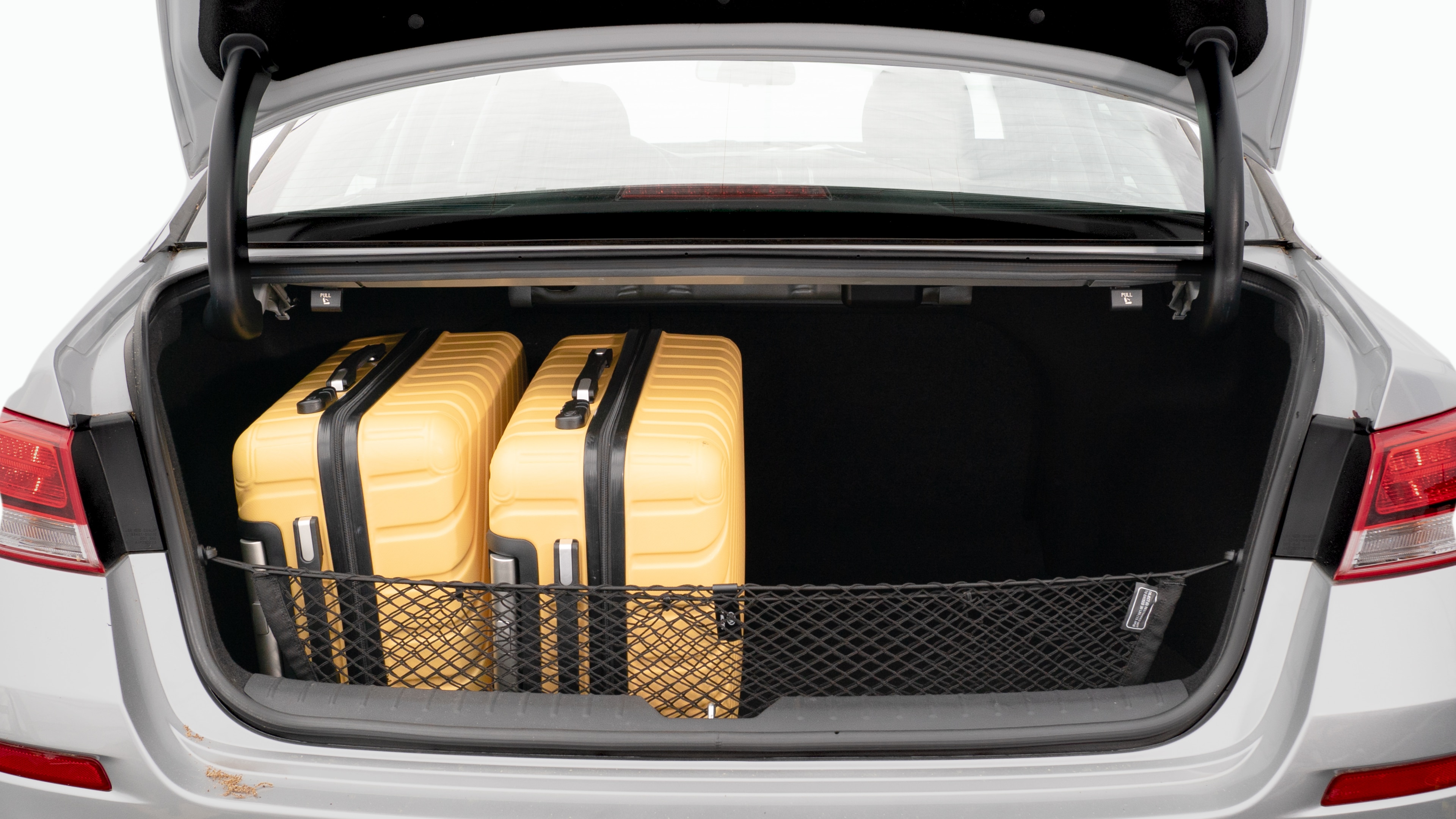 The trunk lid is open, showing a full view of the trunk space. Two large and two small suitcases are placed on there side.