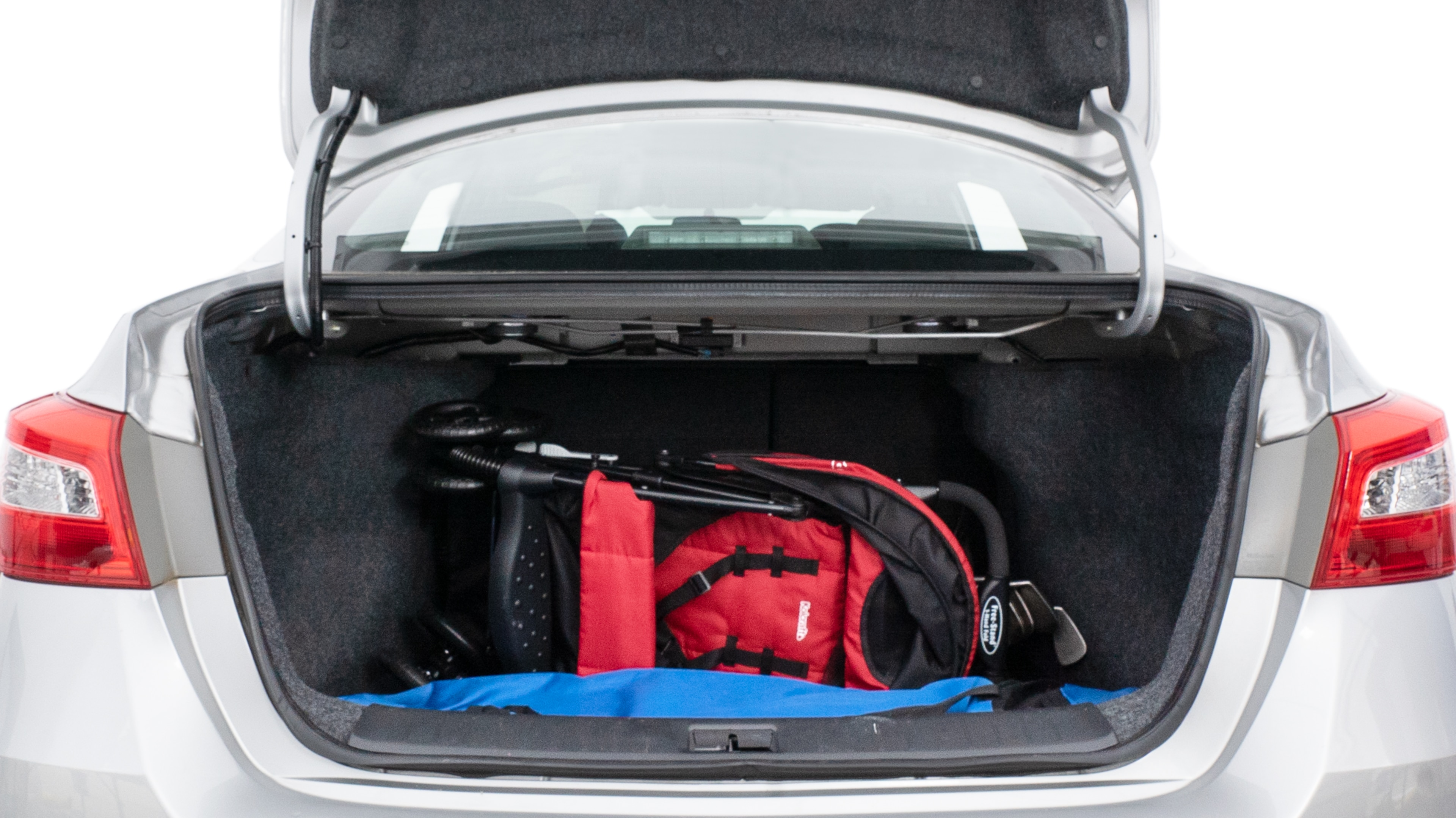 The trunk lid is open showing full view of the trunk. A baby stroller, three grocery carriers, two camping chairs in the carrying bag, and a set of golf clubs are placed inside.