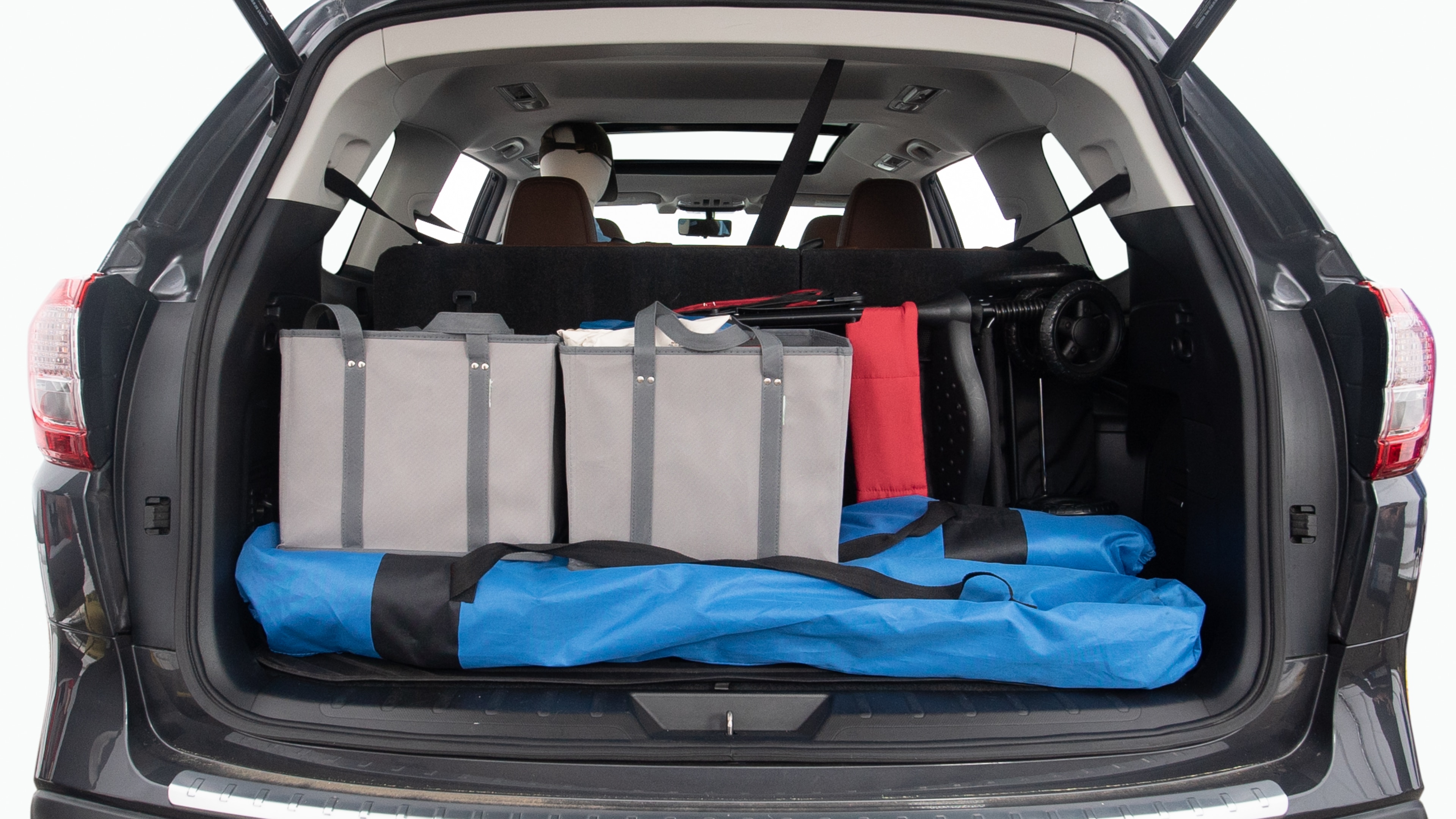 The trunk lid is open showing full view of the trunk. Two grocery carriers, two camping chairs in the carrying bag, and a set of golf clubs are placed inside.