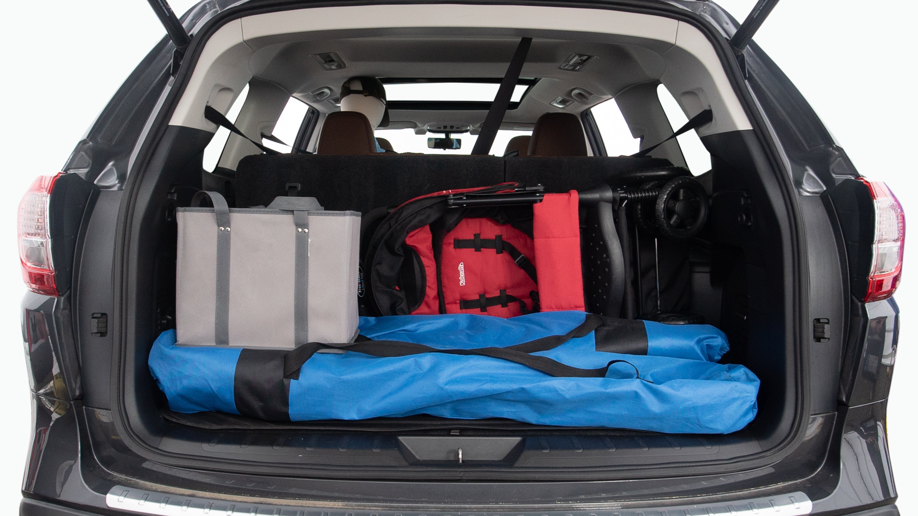 The trunk lid is open showing full view of the trunk. Two grocery carriers, two camping chairs in the carrying bag, and a set of golf clubs are placed inside.