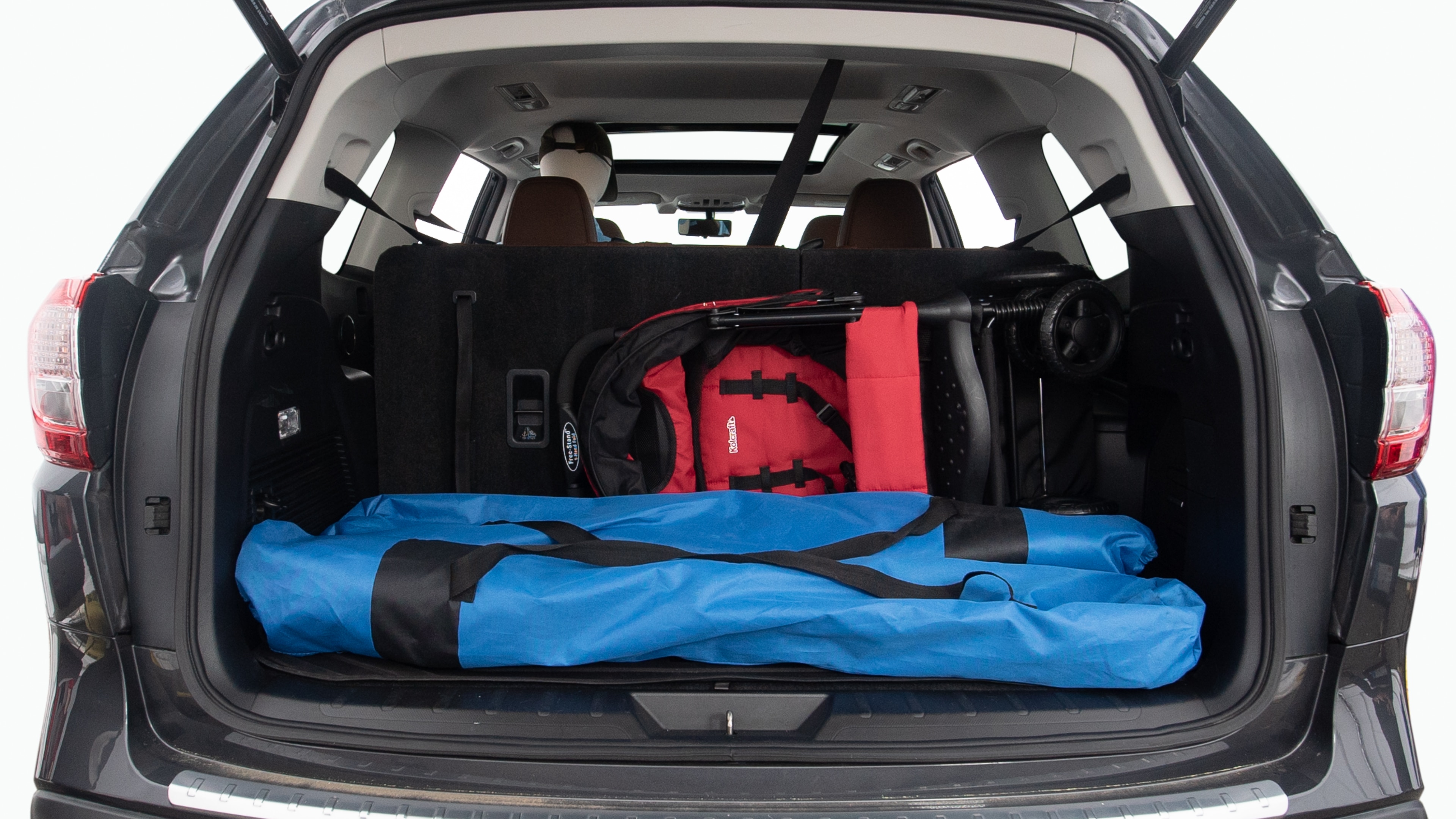 The trunk lid is open showing full view of the trunk. Two grocery carriers, two camping chairs in the carrying bag, and a set of golf clubs are placed inside.