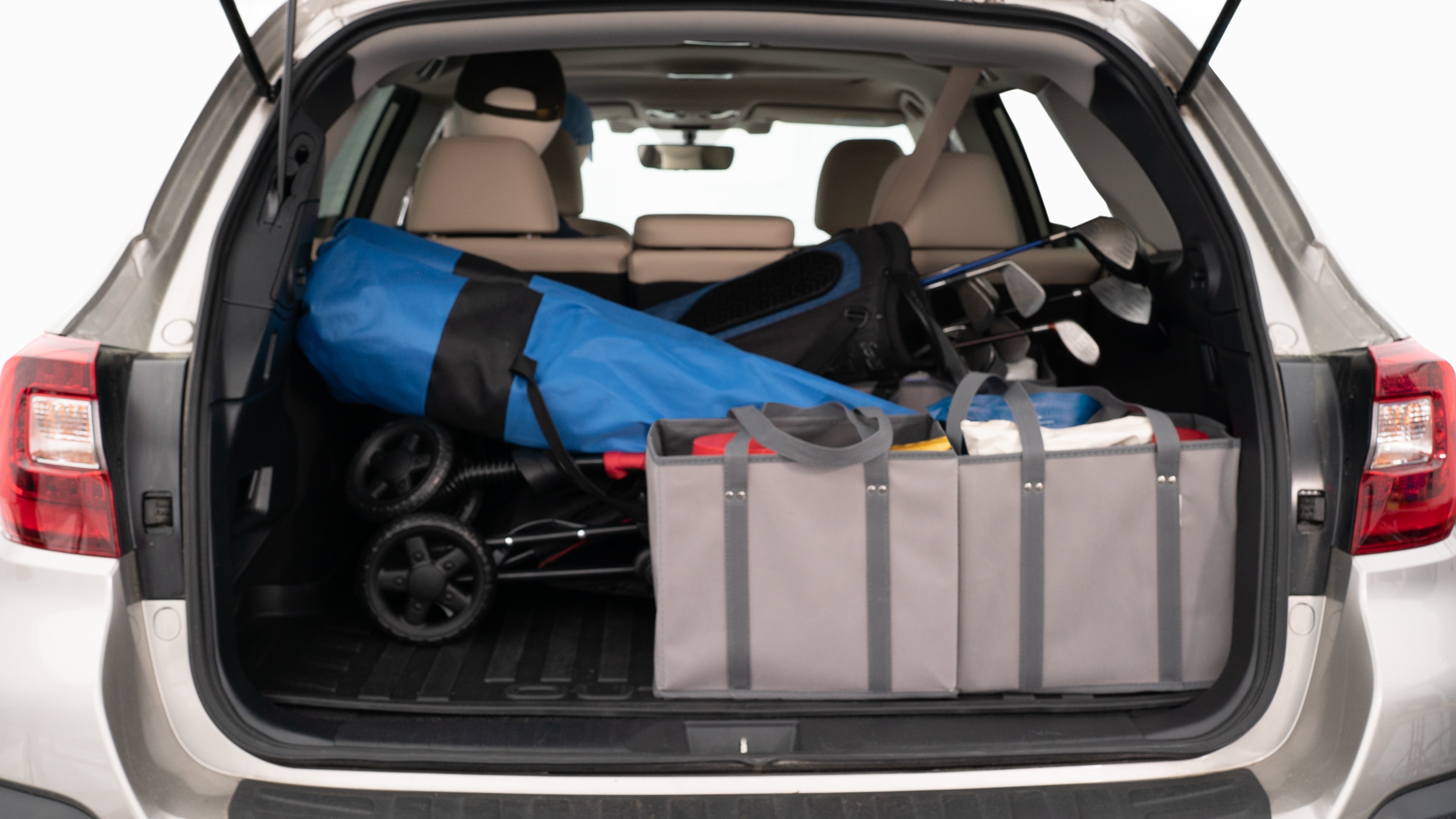 The trunk lid is open showing full view of the trunk. A baby stroller, three grocery carriers, two camping chairs in the carrying bag, and a set of golf clubs are placed inside.