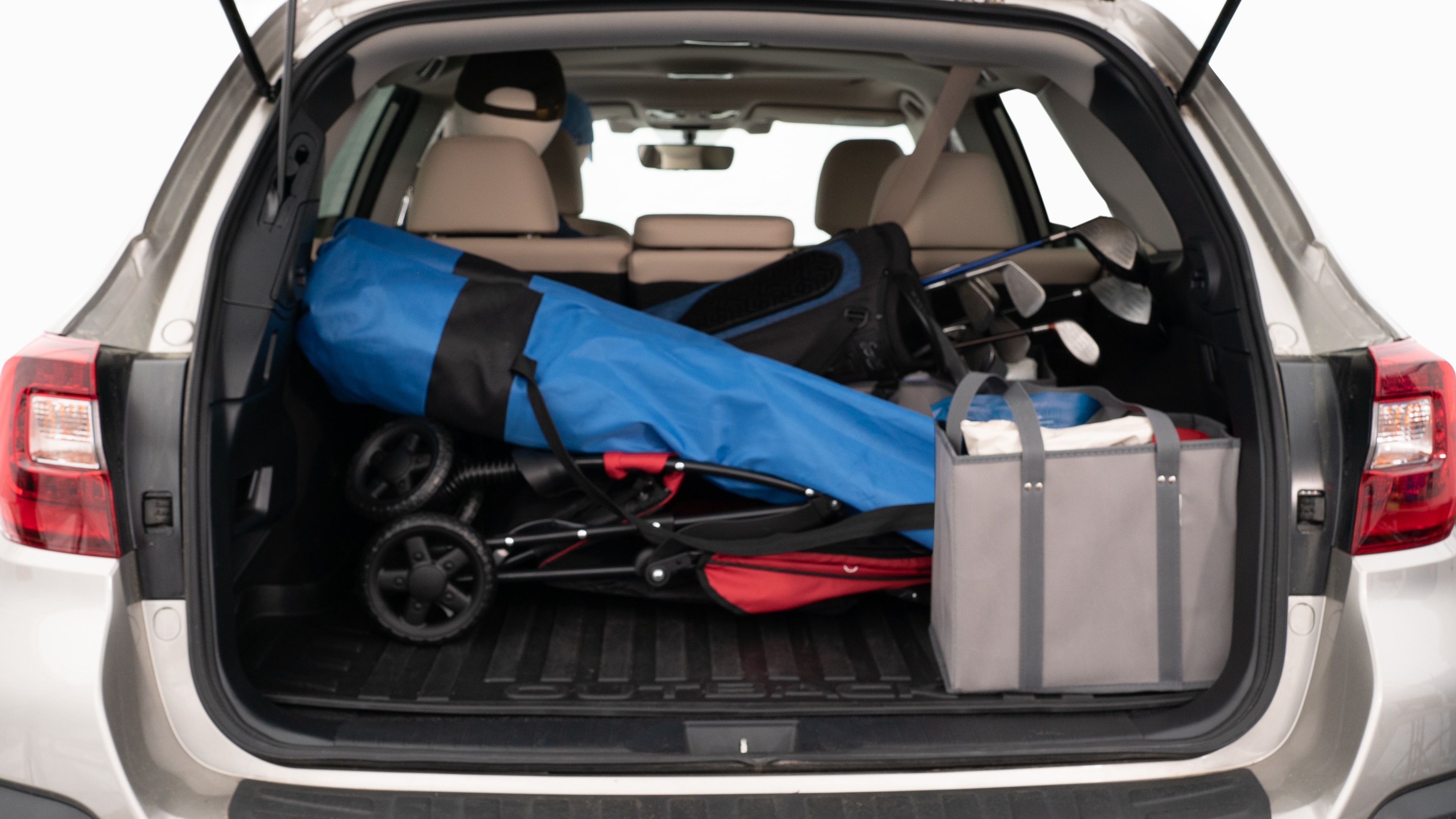The trunk lid is open showing full view of the trunk. A baby stroller, three grocery carriers, two camping chairs in the carrying bag, and a set of golf clubs are placed inside.
