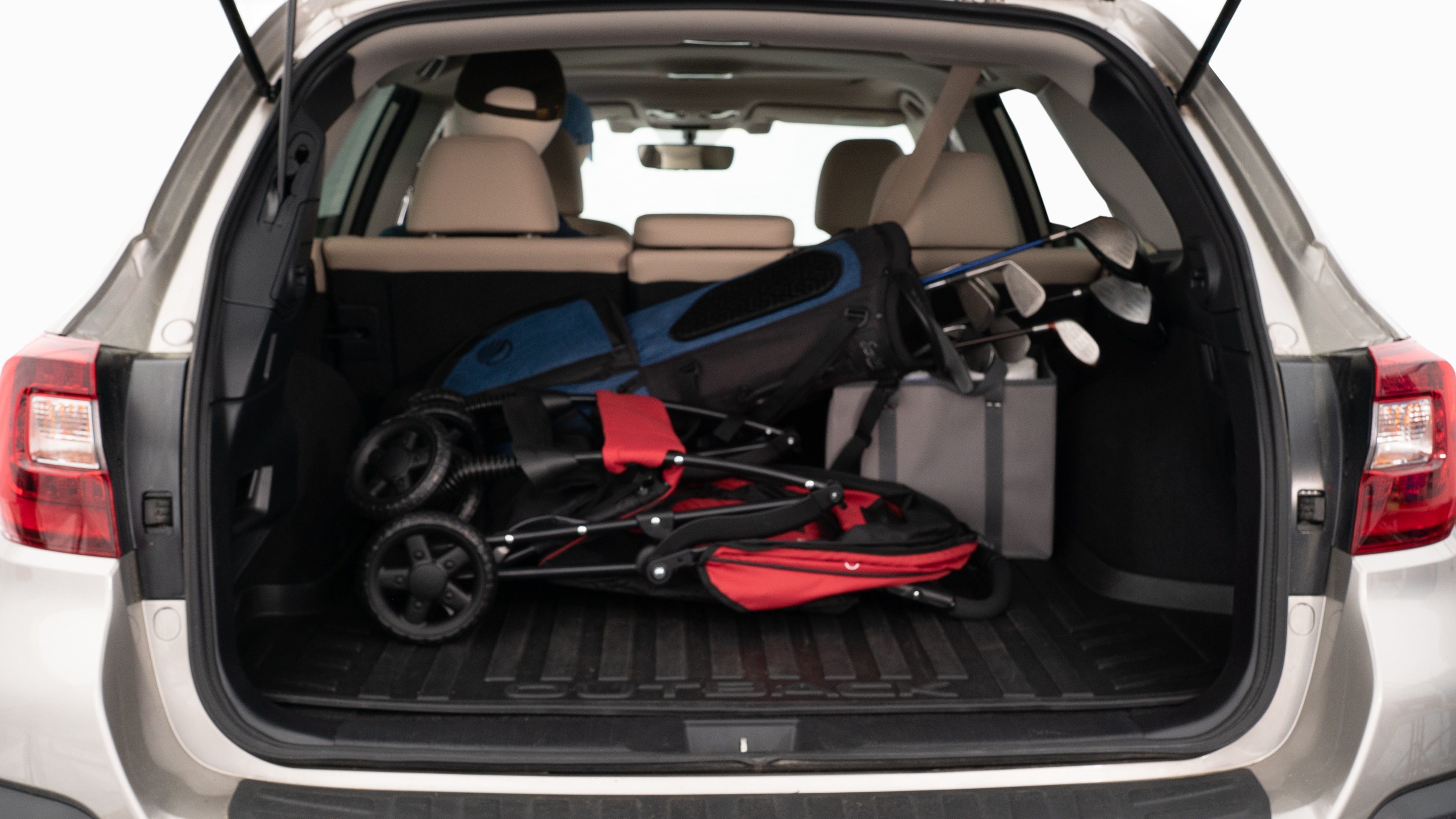 The trunk lid is open showing full view of the trunk. A baby stroller, three grocery carriers, two camping chairs in the carrying bag, and a set of golf clubs are placed inside.