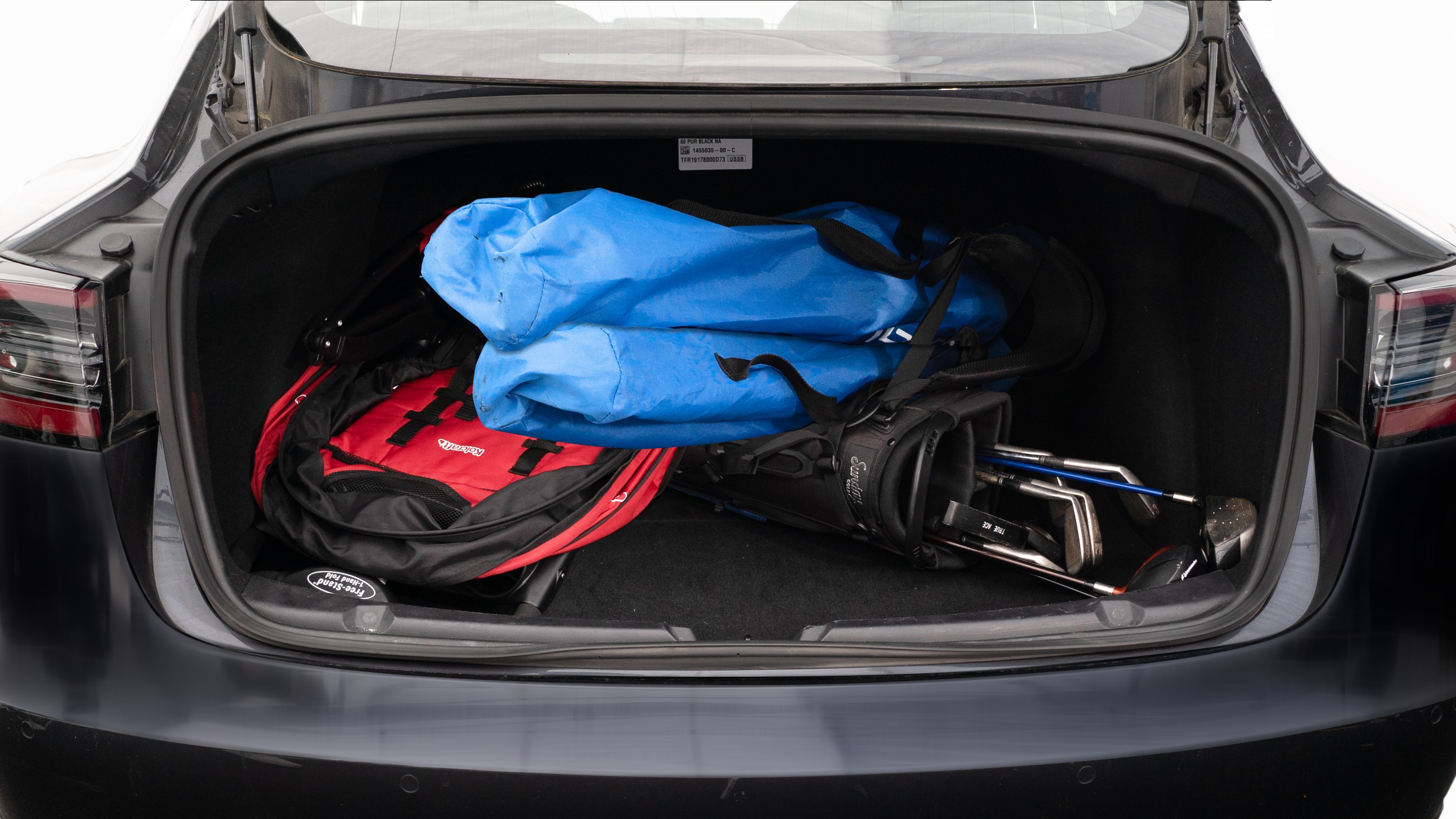 The trunk lid is open showing full view of the trunk. A baby stroller, two camping chairs in the carrying bag, and a set of golf clubs are placed inside.