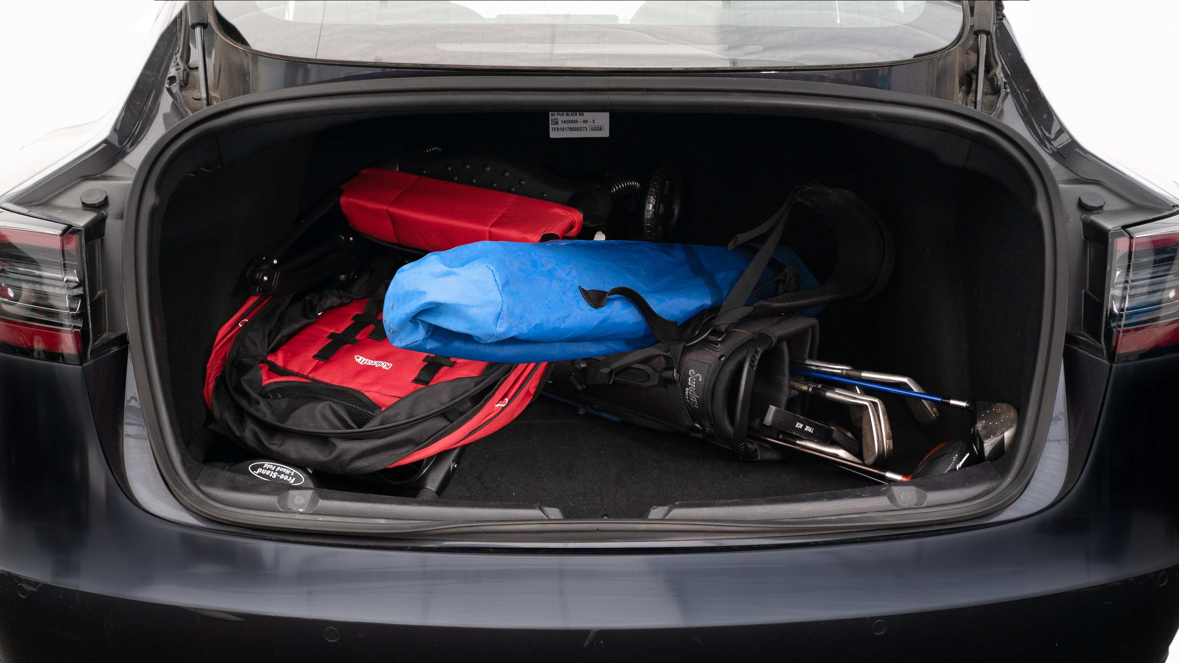 The trunk lid is open showing full view of the trunk. A baby stroller, two camping chairs in the carrying bag, and a set of golf clubs are placed inside.