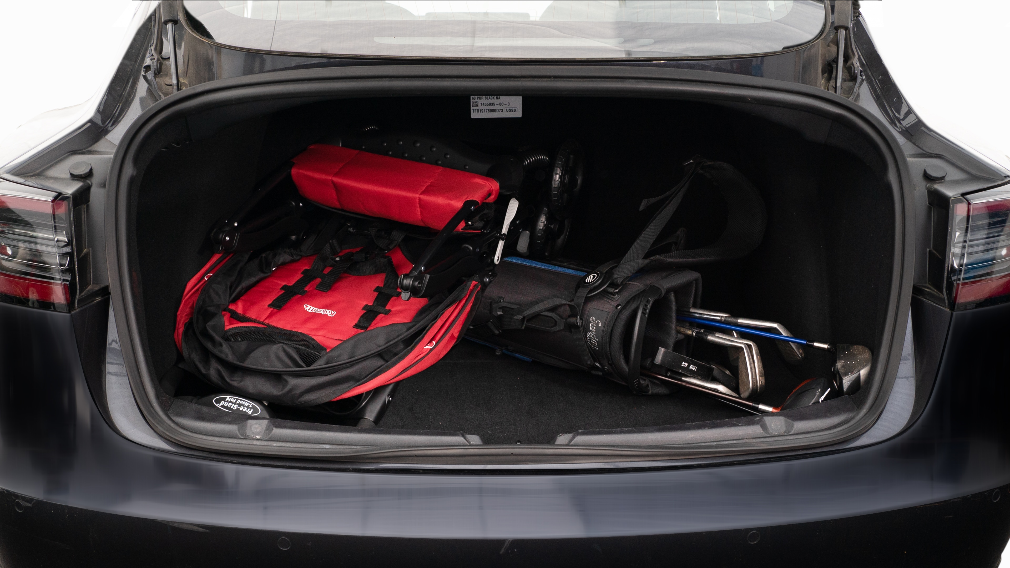The trunk lid is open showing full view of the trunk. A baby stroller, two camping chairs in the carrying bag, and a set of golf clubs are placed inside.