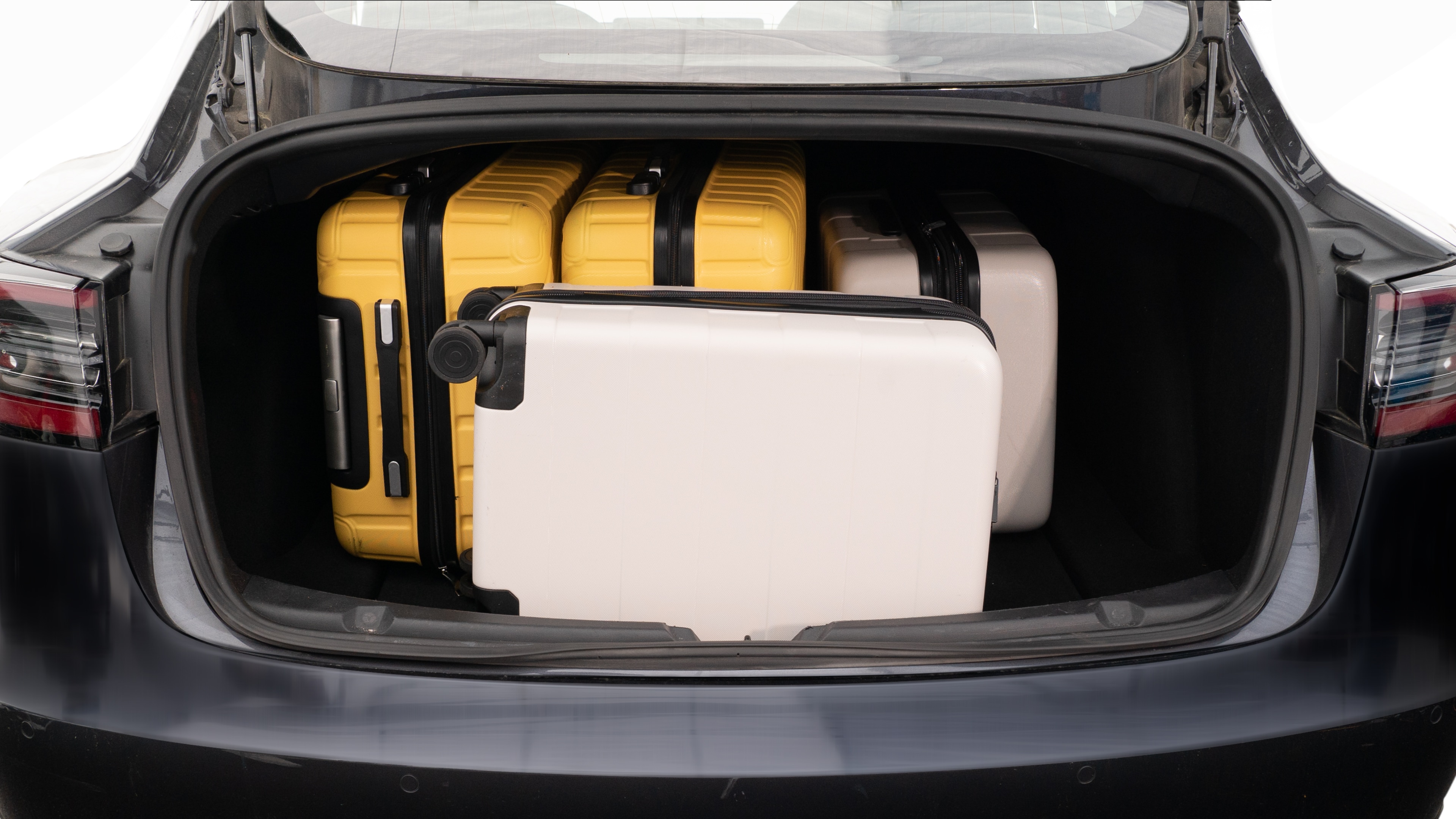 The trunk lid is open, showing a full view of the trunk space. Two large and two small suitcases are placed inside.