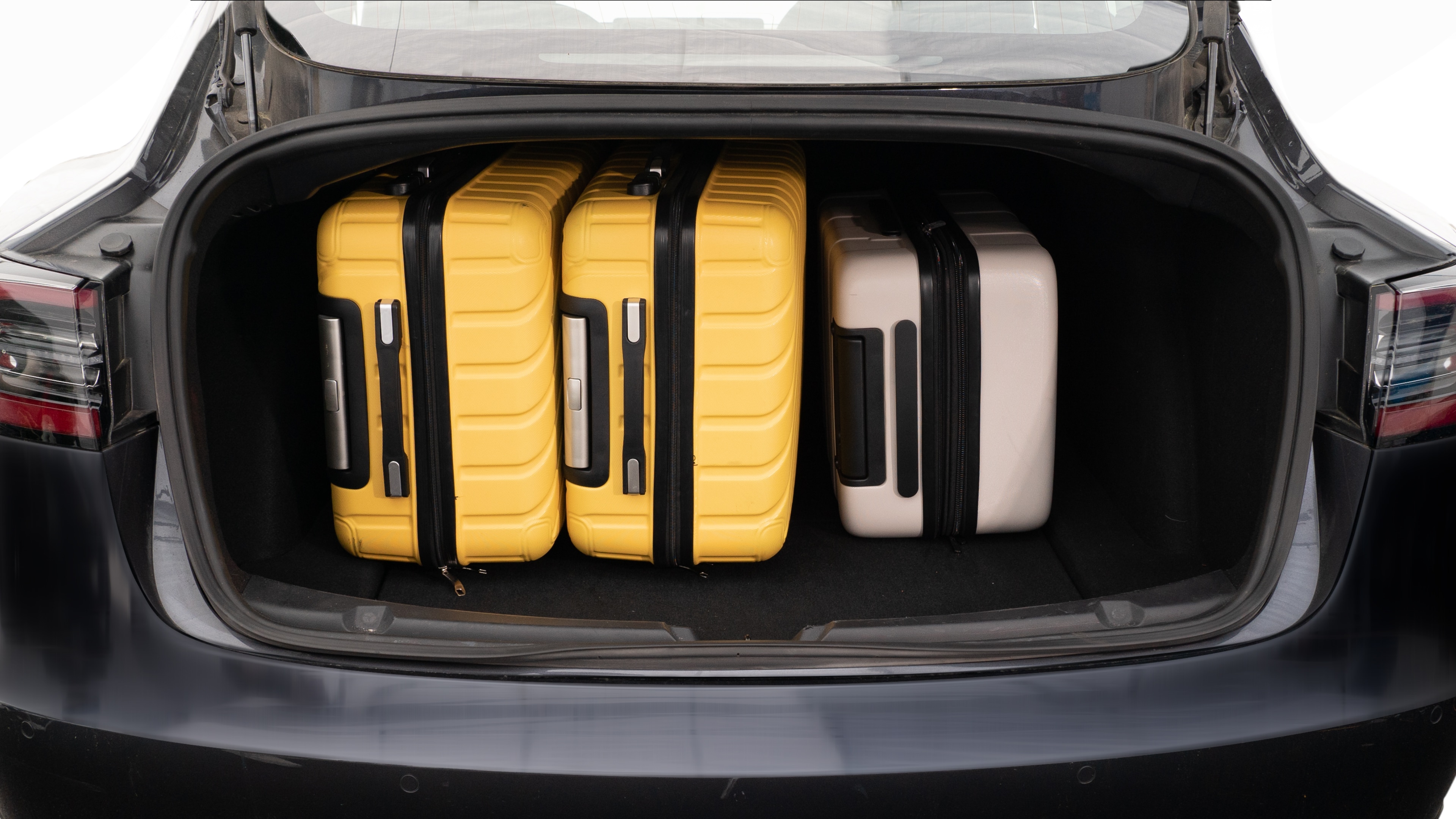 The trunk lid is open, showing a full view of the trunk space. Two large and two small suitcases are placed inside.