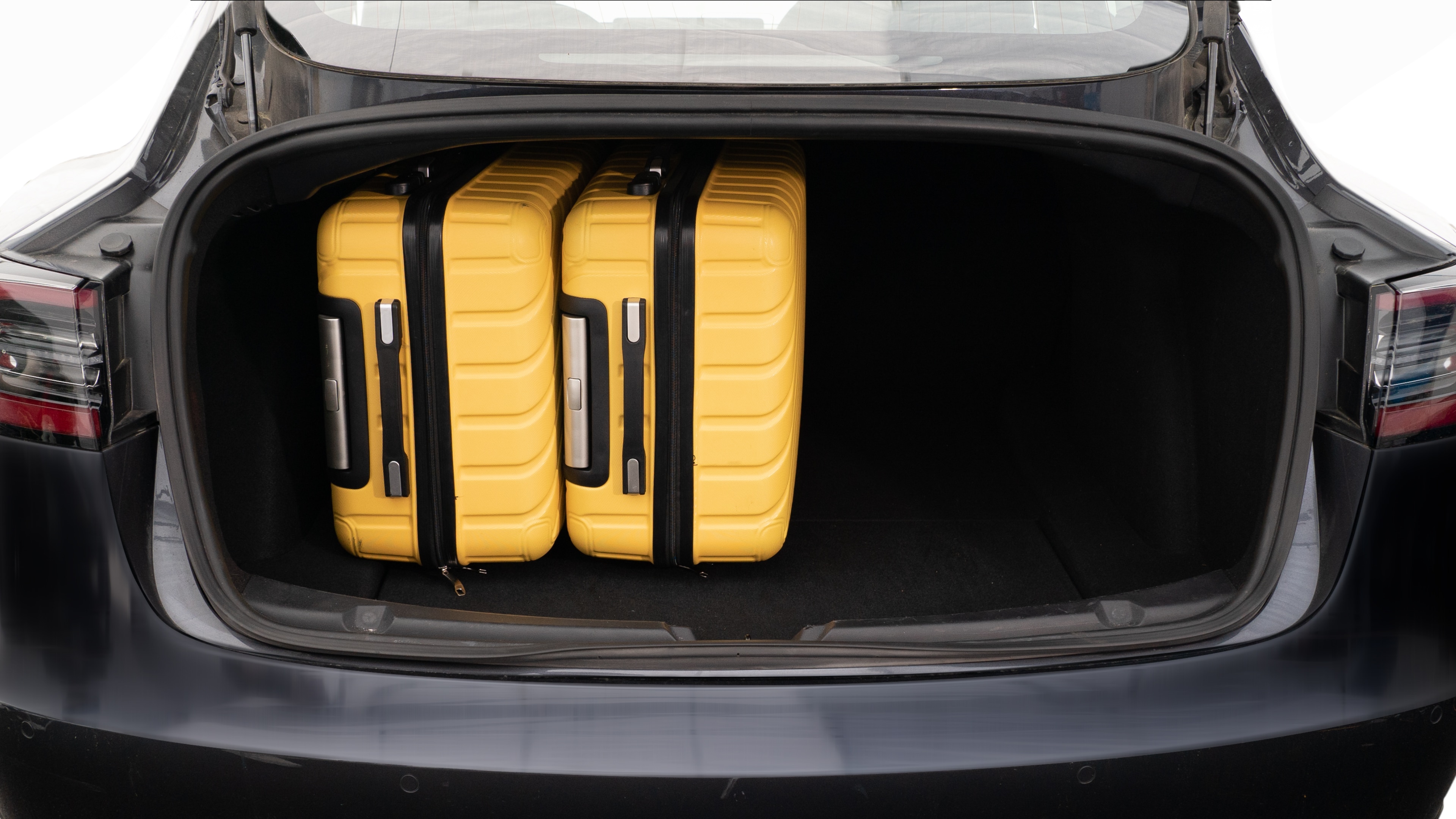 The trunk lid is open, showing a full view of the trunk space. Two large and two small suitcases are placed inside.