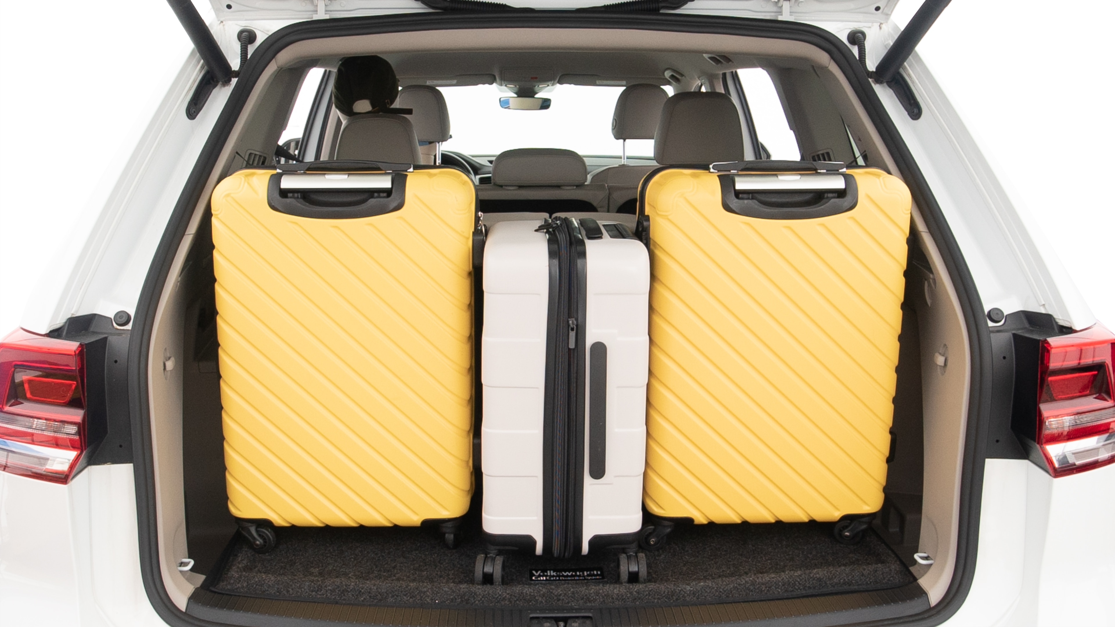 The trunk lid is open, showing full view of the trunk space. Two large and one small suitcases are placed inside.