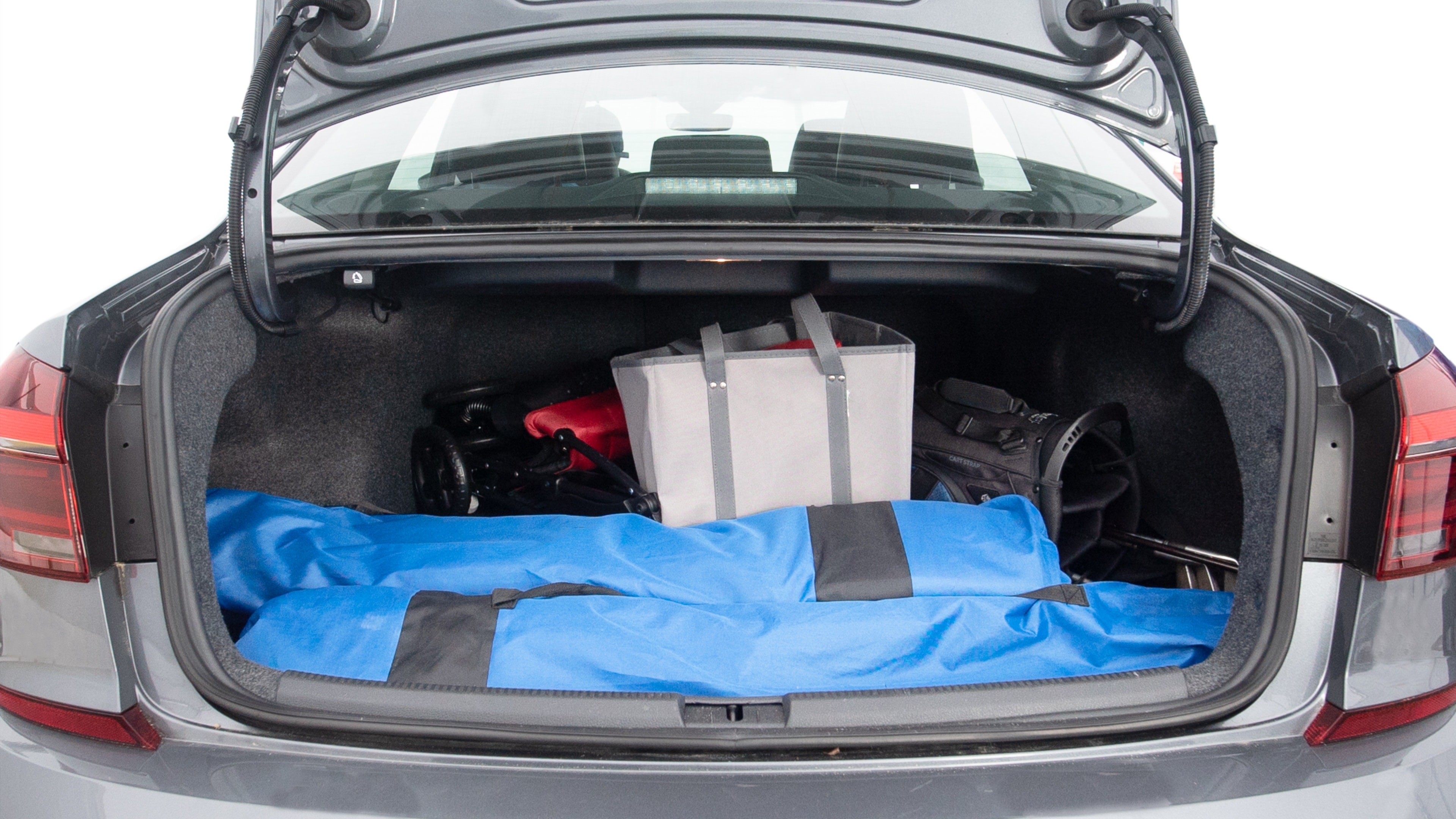 The trunk lid is open showing full view of the trunk. A baby stroller, three grocery carriers, two camping chairs in the carrying bag, and a set of golf clubs are placed inside.