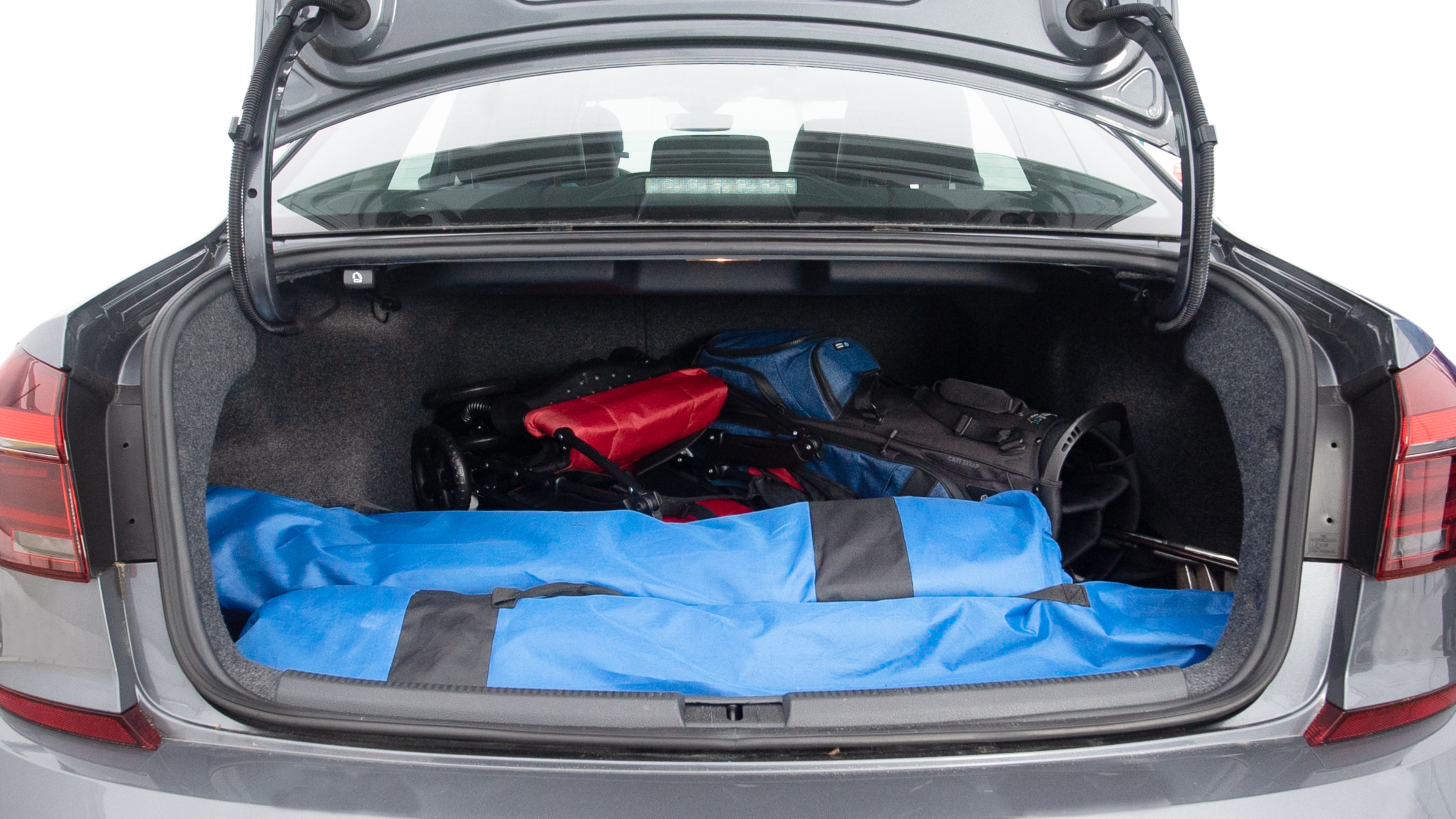 The trunk lid is open showing full view of the trunk. A baby stroller, three grocery carriers, two camping chairs in the carrying bag, and a set of golf clubs are placed inside.