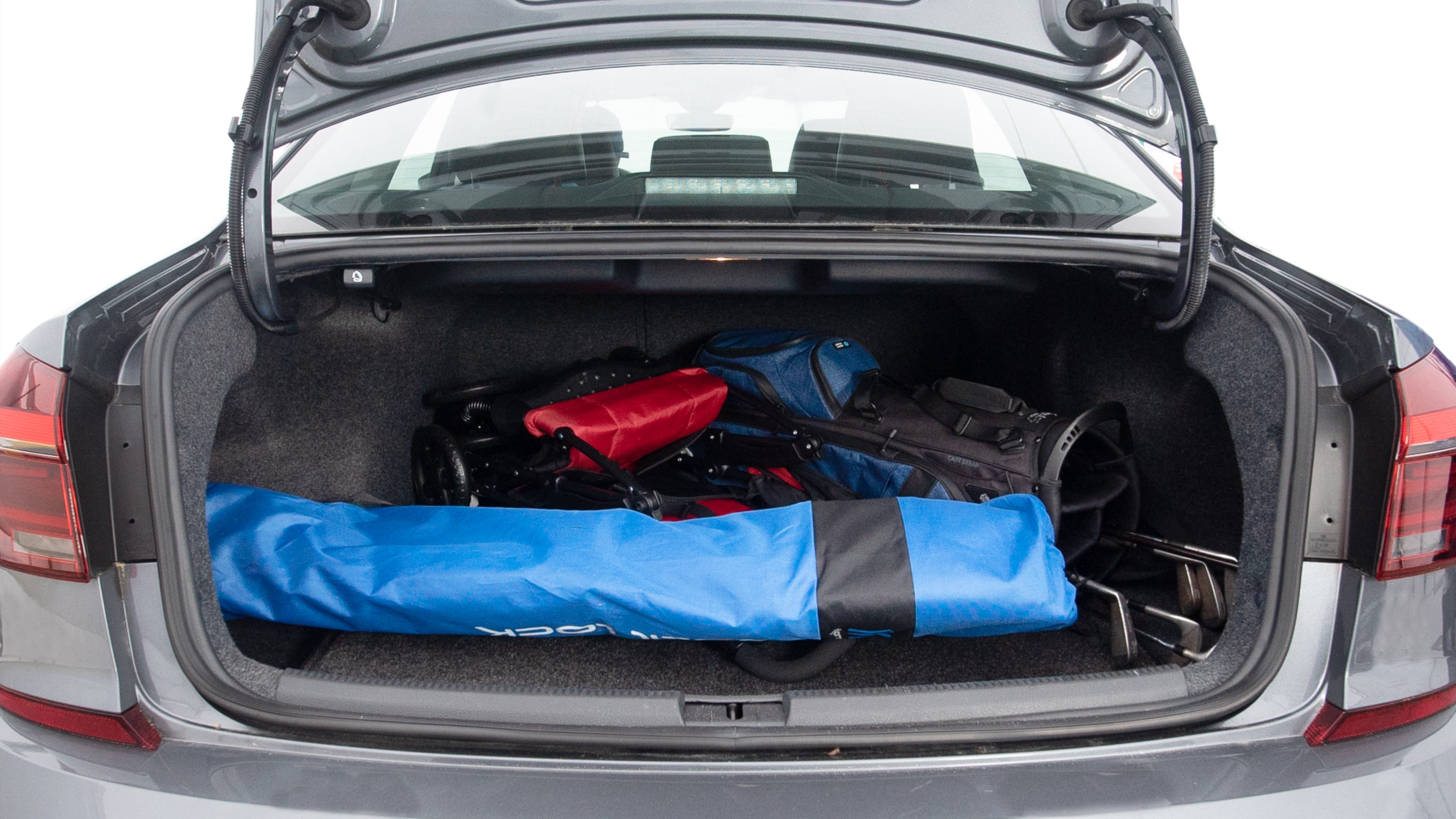 The trunk lid is open showing full view of the trunk. A baby stroller, three grocery carriers, two camping chairs in the carrying bag, and a set of golf clubs are placed inside.