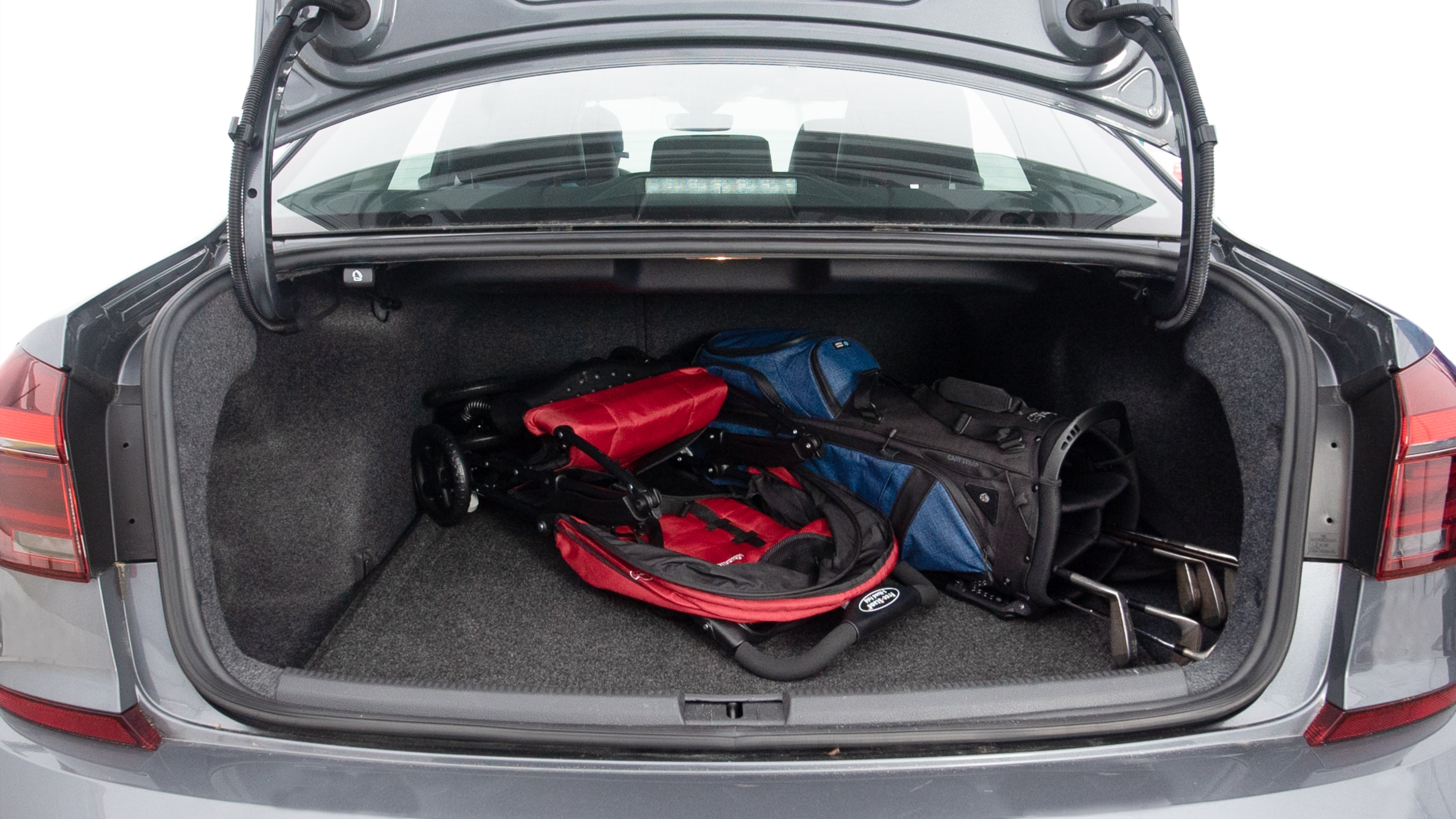 The trunk lid is open showing full view of the trunk. A baby stroller, three grocery carriers, two camping chairs in the carrying bag, and a set of golf clubs are placed inside.