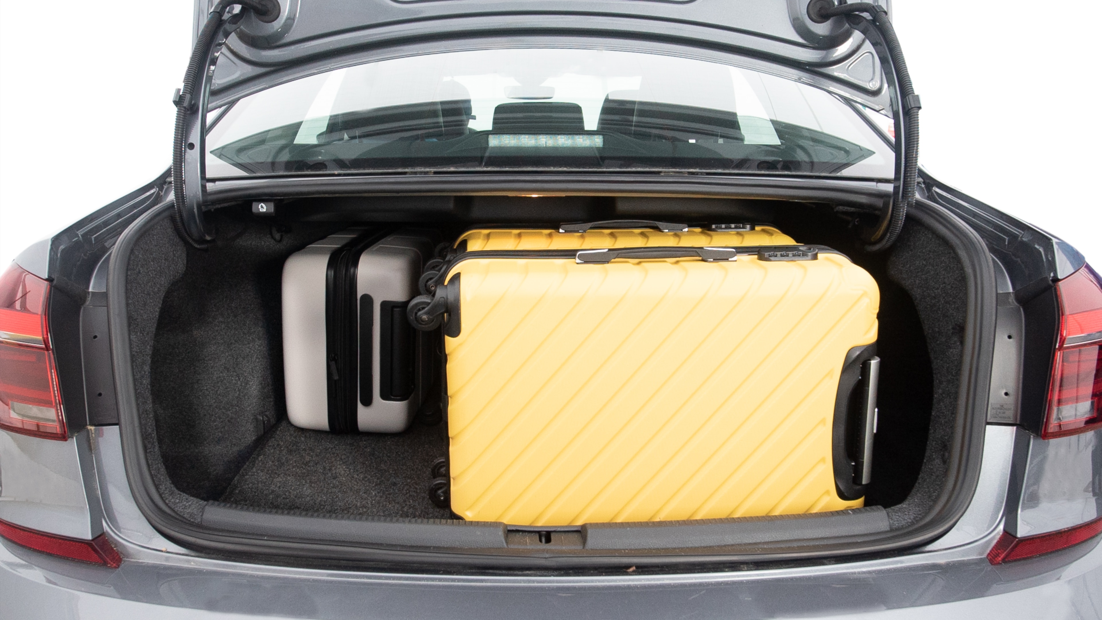 The trunk lid is open, showing full view of the trunk space. Three large and one small suitcases are placed inside.