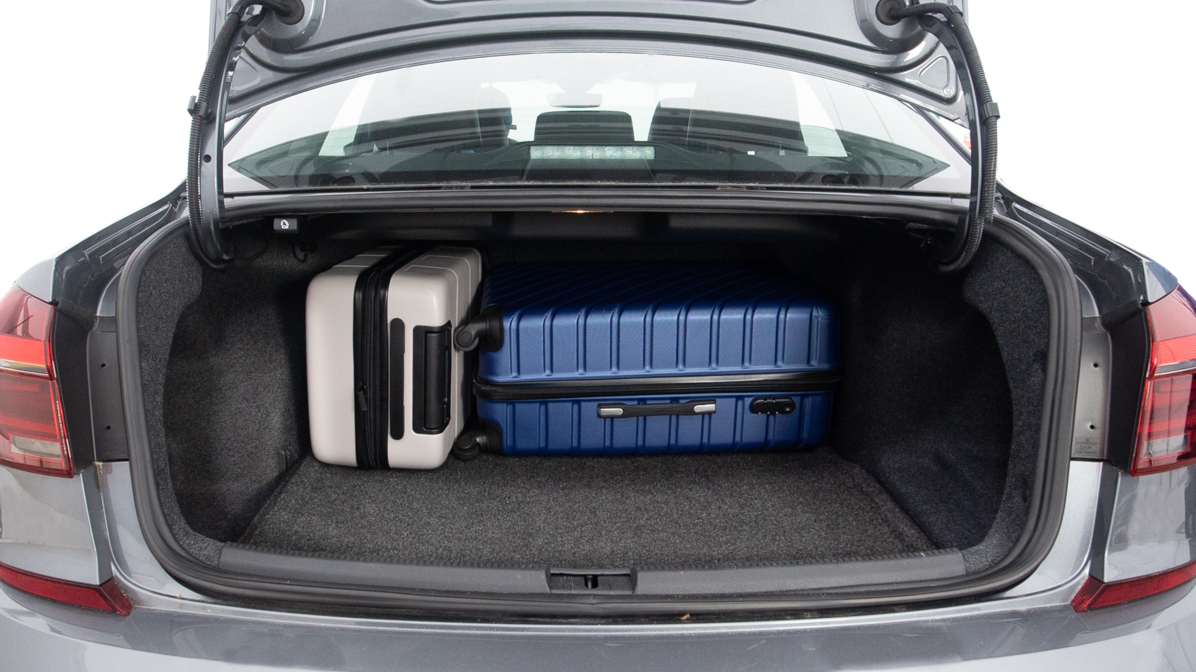 The trunk lid is open, showing full view of the trunk space. Three large and one small suitcases are placed inside.