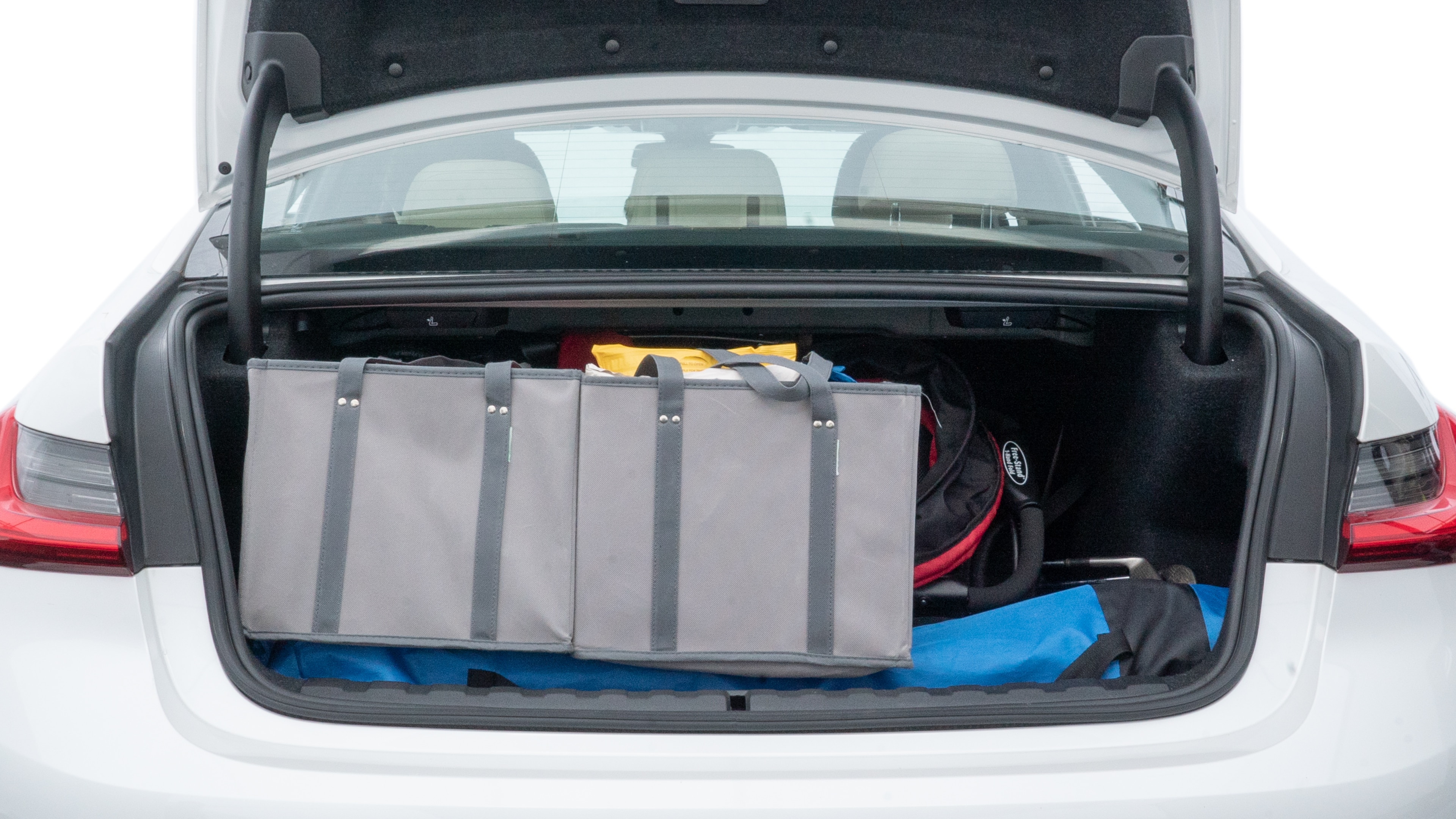 The trunk lid is open showing full view of the trunk. A baby stroller, three grocery carriers, two camping chairs in the carrying bag, and a set of golf clubs are placed inside.