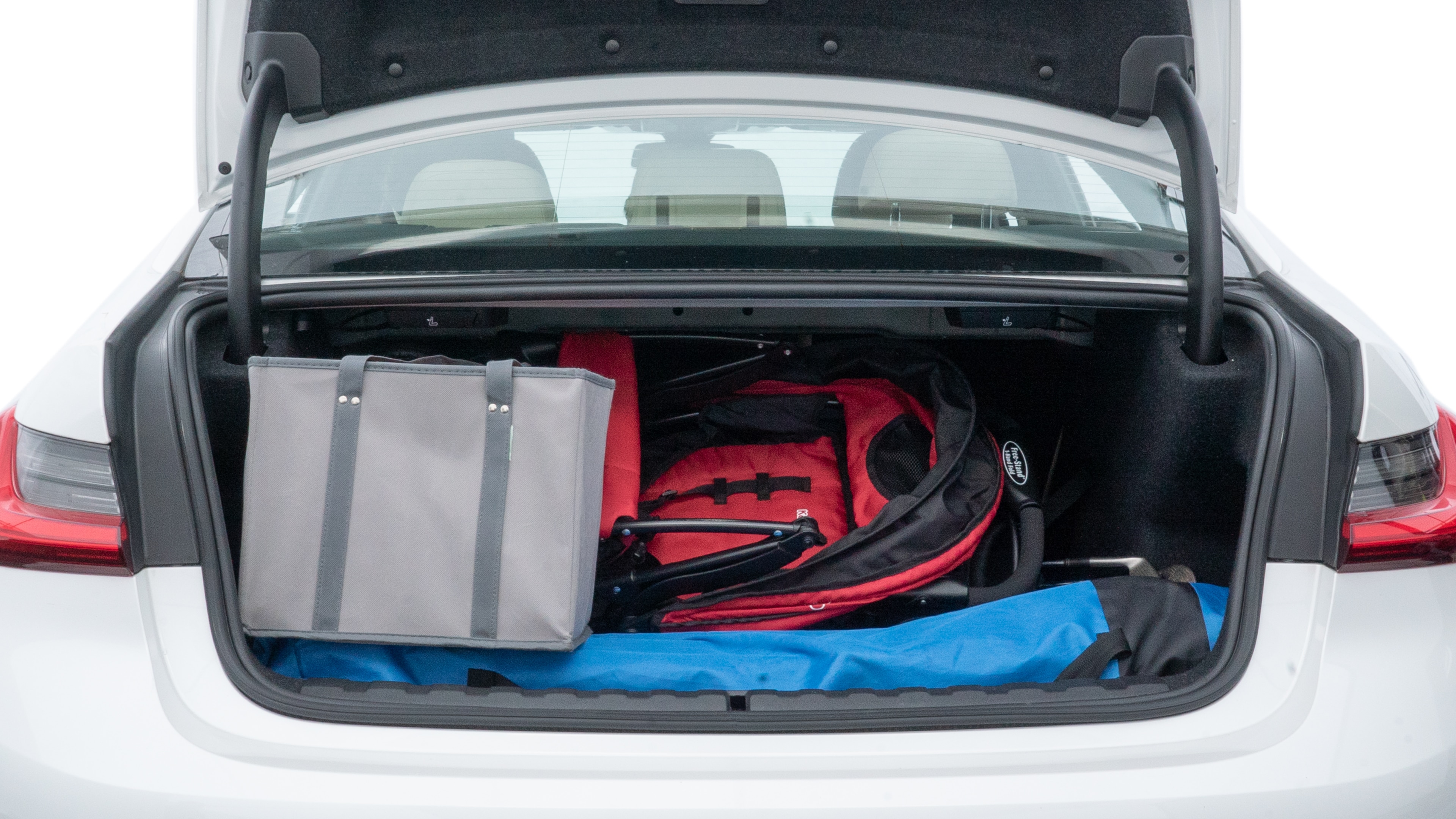 The trunk lid is open showing full view of the trunk. A baby stroller, three grocery carriers, two camping chairs in the carrying bag, and a set of golf clubs are placed inside.