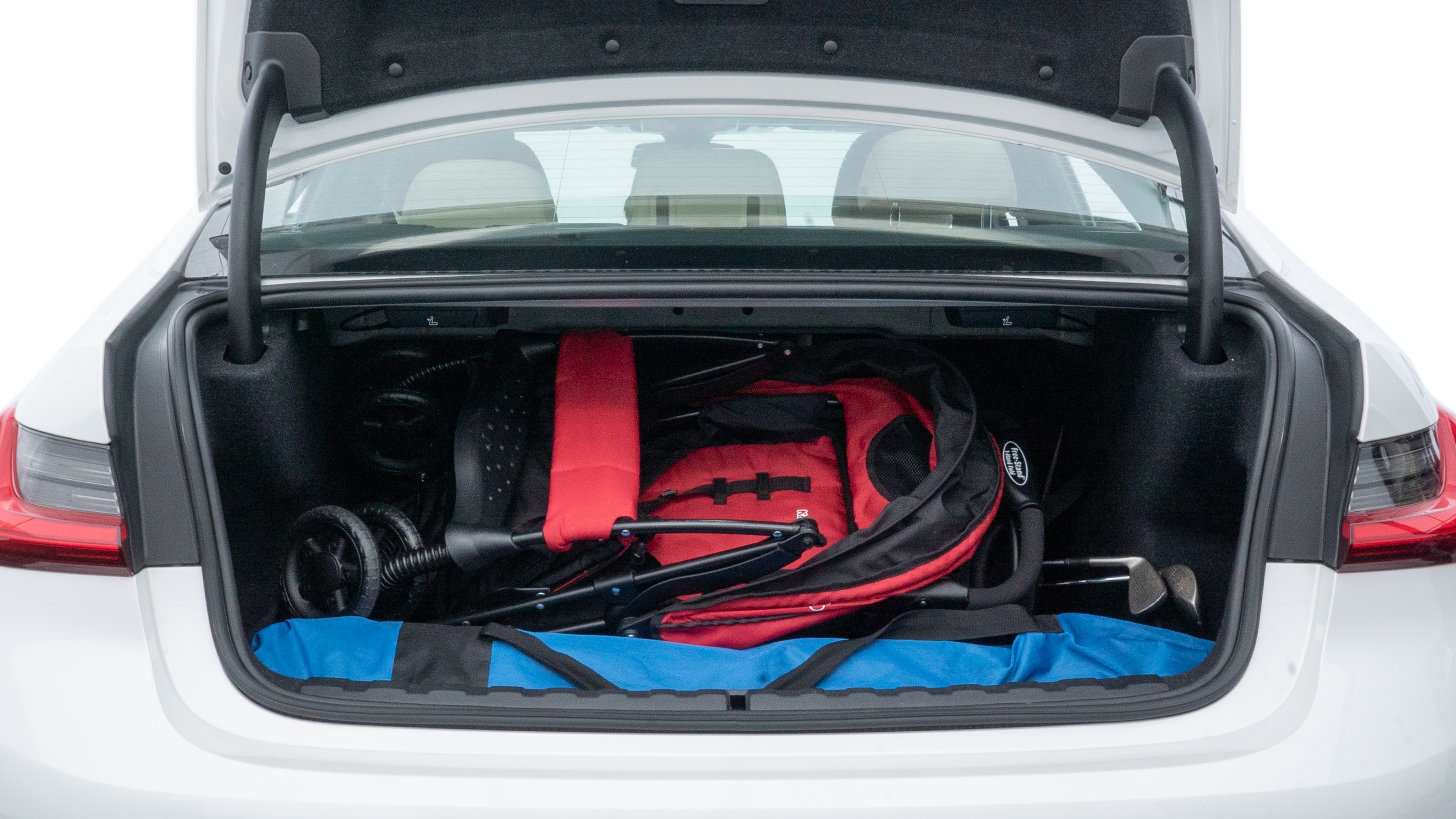 The trunk lid is open showing full view of the trunk. A baby stroller, three grocery carriers, two camping chairs in the carrying bag, and a set of golf clubs are placed inside.