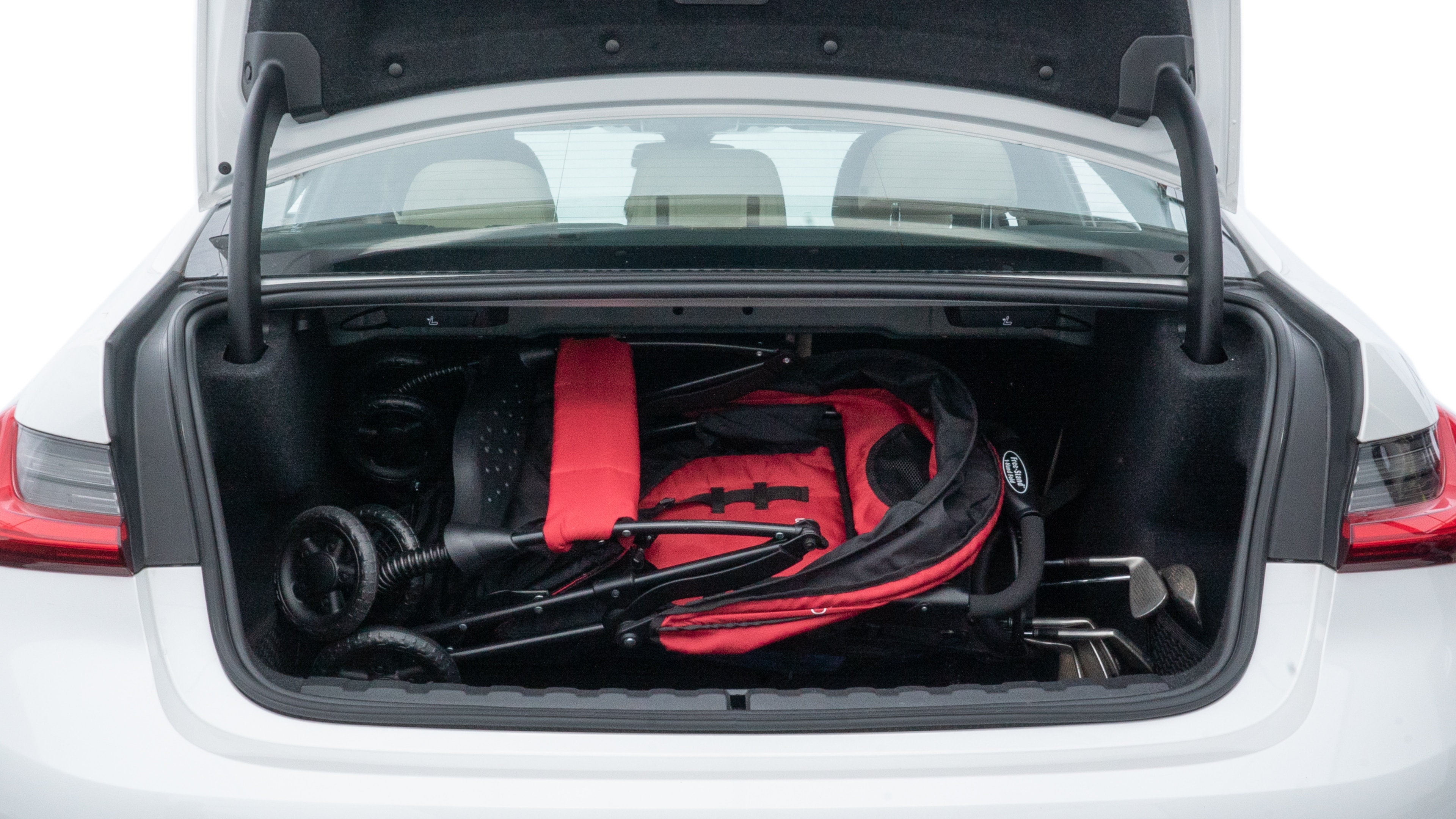 The trunk lid is open showing full view of the trunk. A baby stroller, three grocery carriers, two camping chairs in the carrying bag, and a set of golf clubs are placed inside.