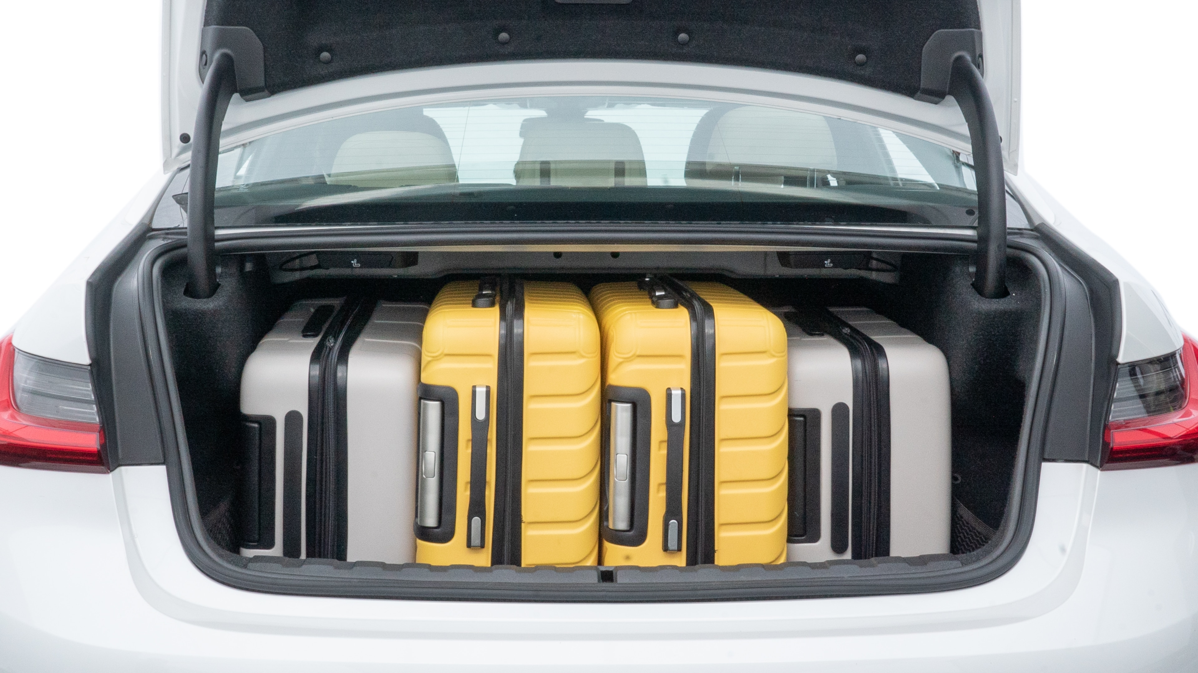 The trunk lid is open, showing full view of the trunk space. One large, two medium, and two small suitcases are placed inside.