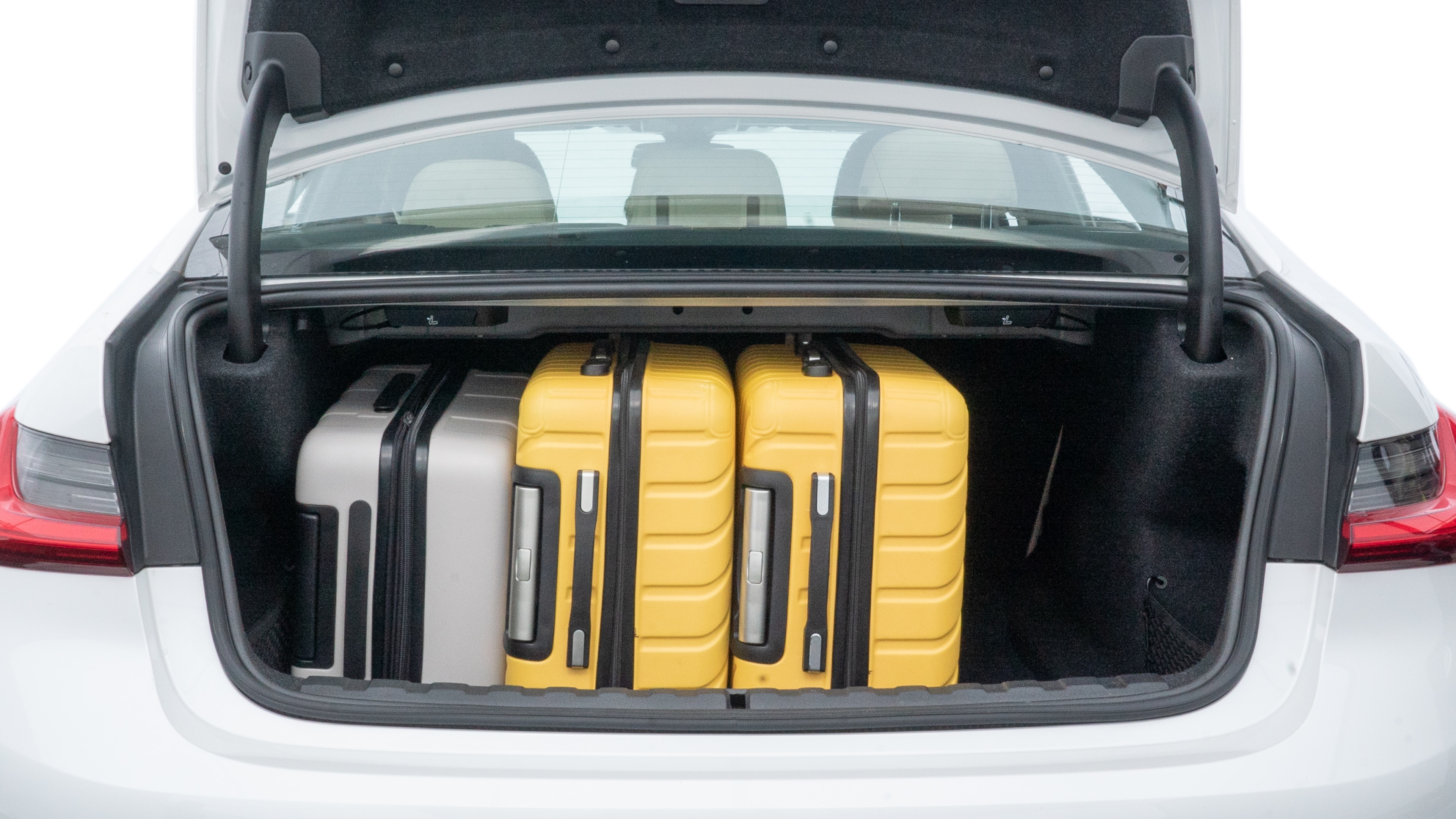 The trunk lid is open, showing full view of the trunk space. One large, two medium, and two small suitcases are placed inside.